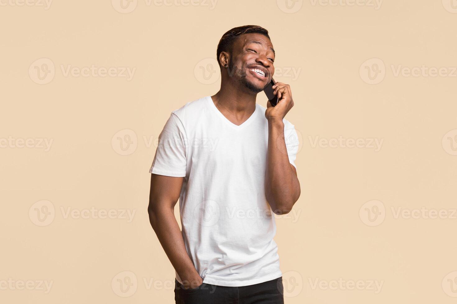 Phone Call. Positive Black Man Talking On Cellphone And Laughing Standing Over Yellow Background. Studio Shot photo