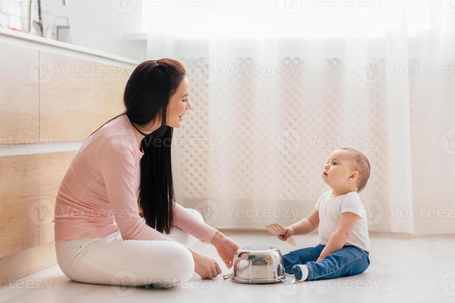 A woman is seated on the floor beside a baby, engaging in a close interaction. The woman appears attentive to the baby needs, providing care and support in a nurturing manner. photo