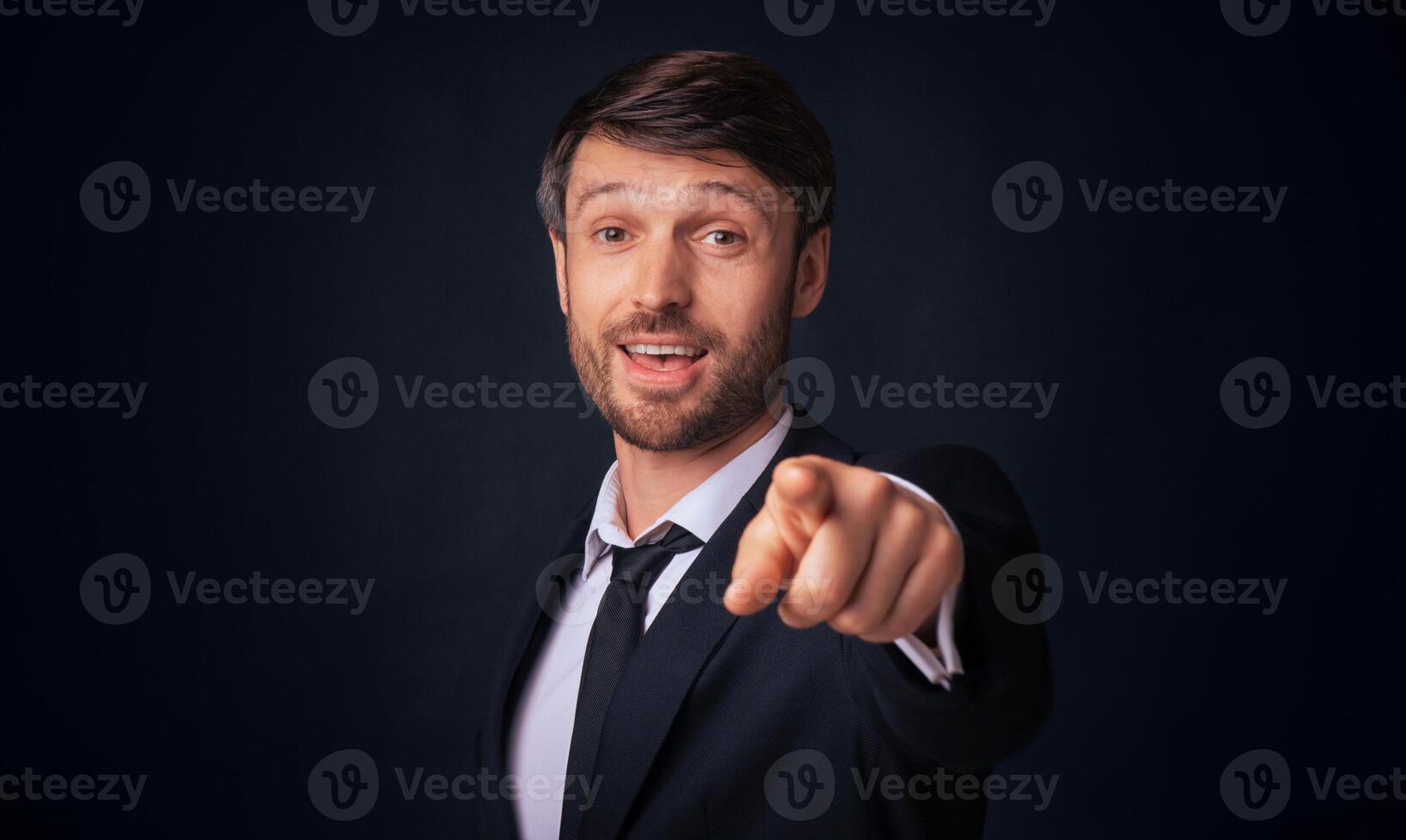 Hey, You. Businessman Pointing Finger At Camera Standing On Black Studio Background. Copy Space photo