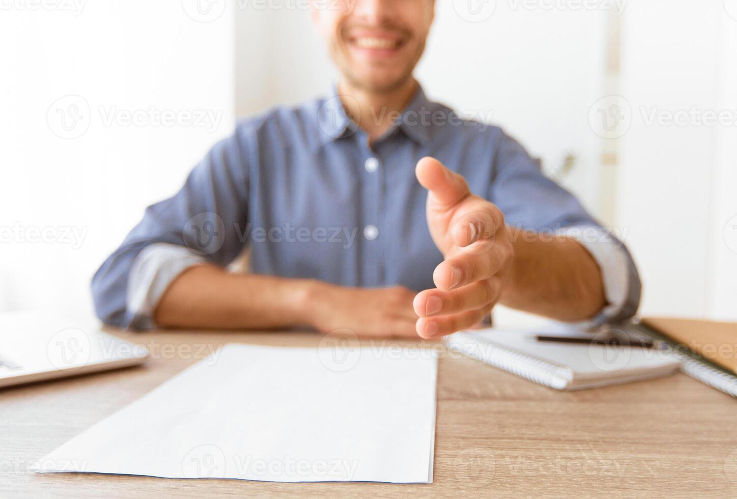 A man sitting at a desk extends his hand for a handshake, with a smile on his face. photo