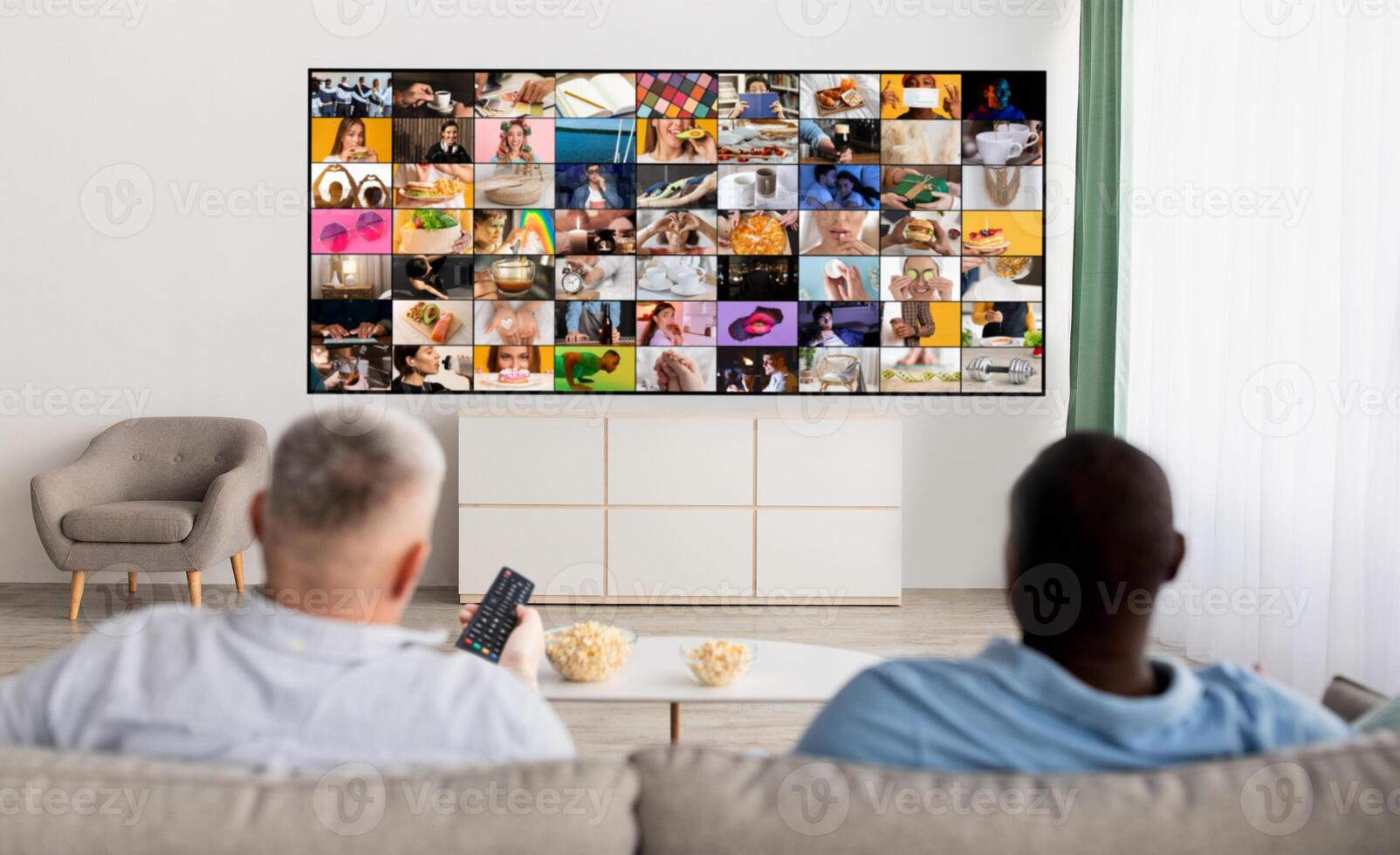 Two people are sitting on a couch in a living room, watching a large television screen displaying a multitude of smaller screens. They appear to be engrossed in the content displayed on the television photo