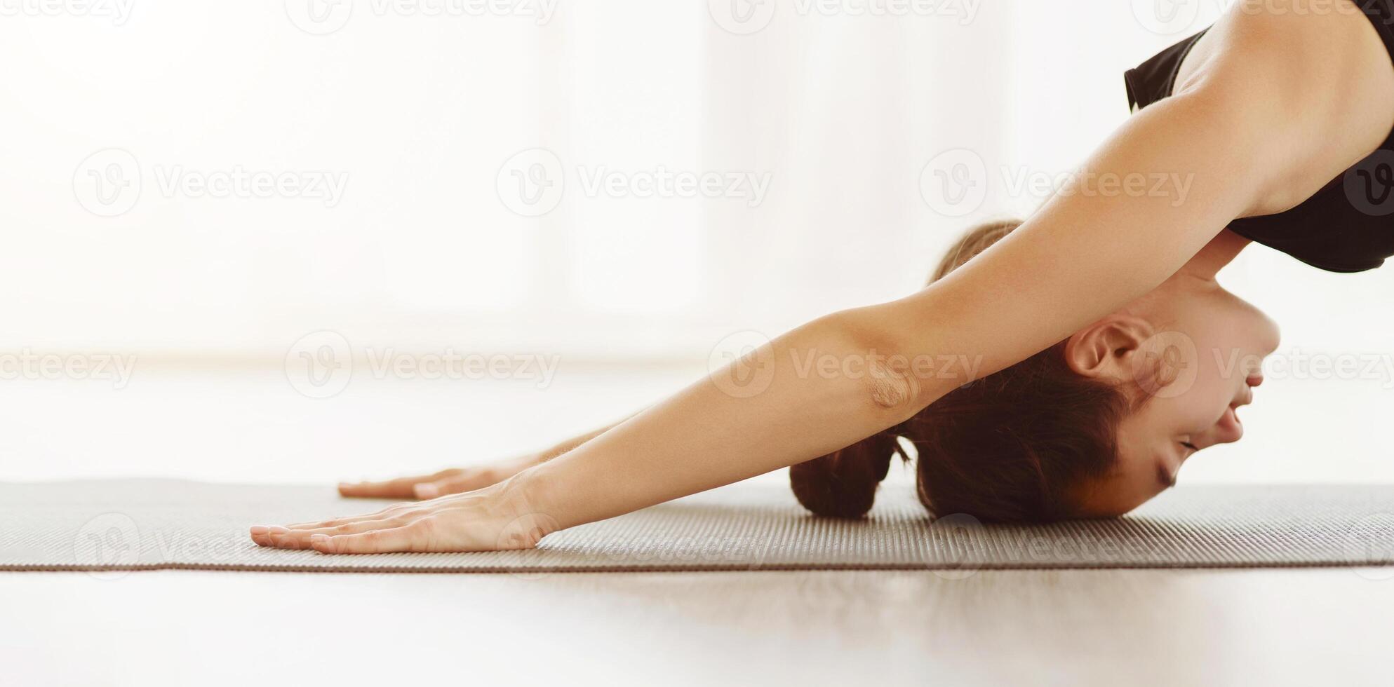 A woman is engaged in a yoga session, executing the Downward Facing Dog pose with precision and focus. Her hands are firmly planted on a yoga mat, closeup, panorama with copy space photo