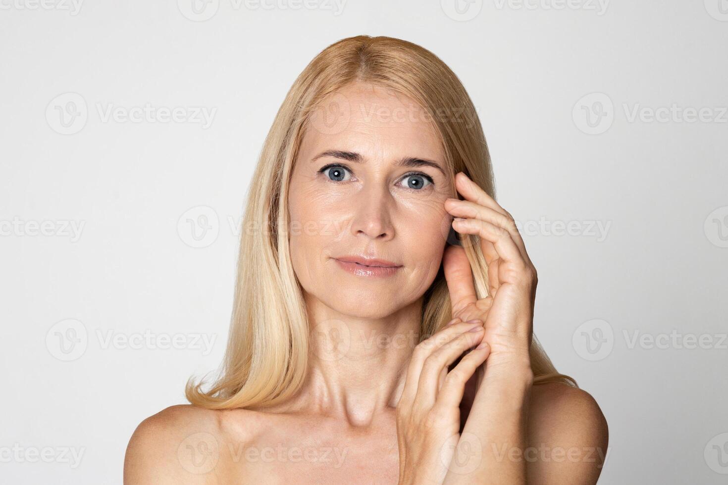 This image shows a portrait of a blonde woman with blue eyes. She is wearing no makeup and her skin appears to be naturally flawless. The woman is looking directly at the camera photo