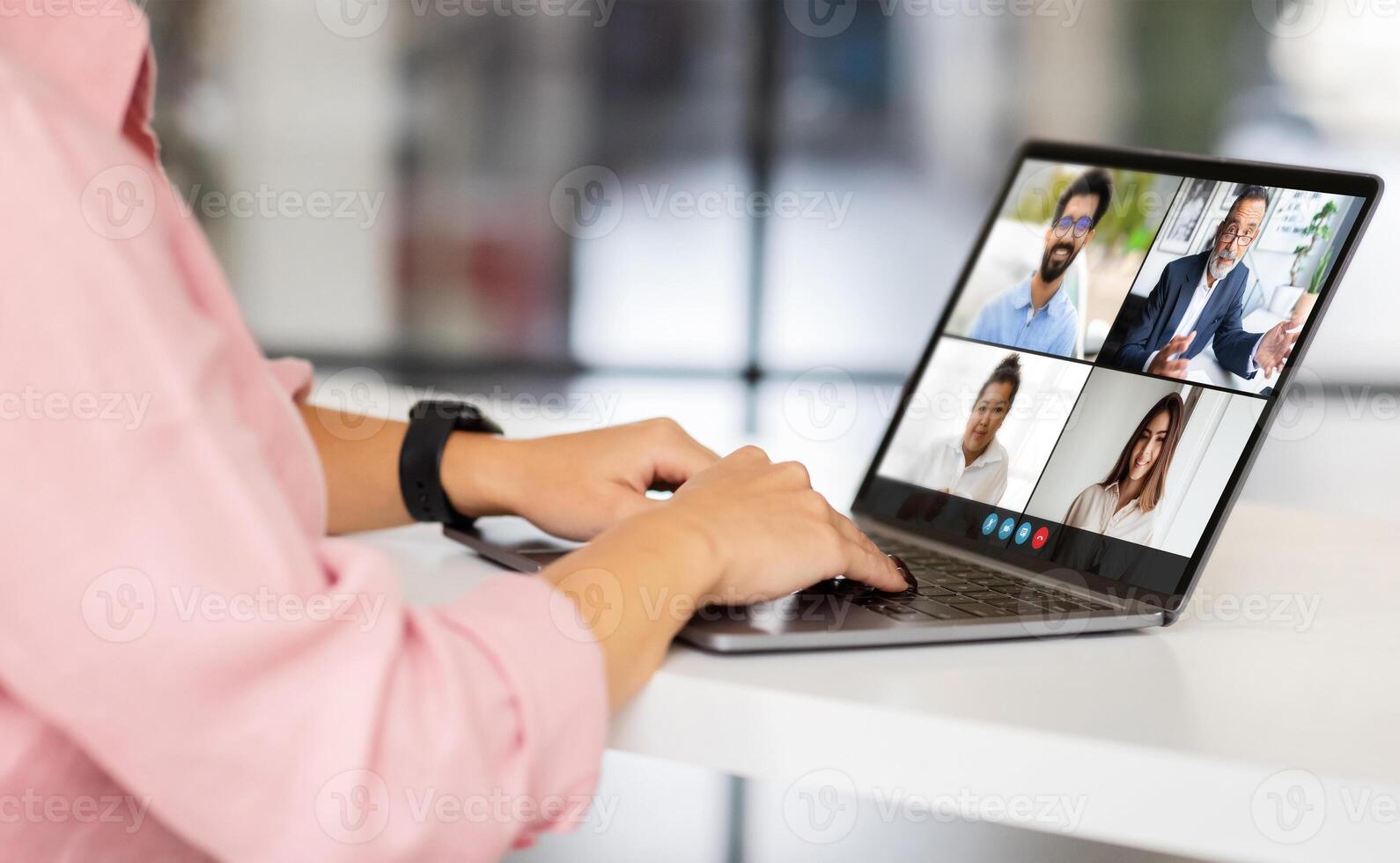 Woman coach using a laptop computer to participate in a call with a group of colleagues. The woman is sitting at a desk in an office and is using a laptop to chat with her colleagues photo