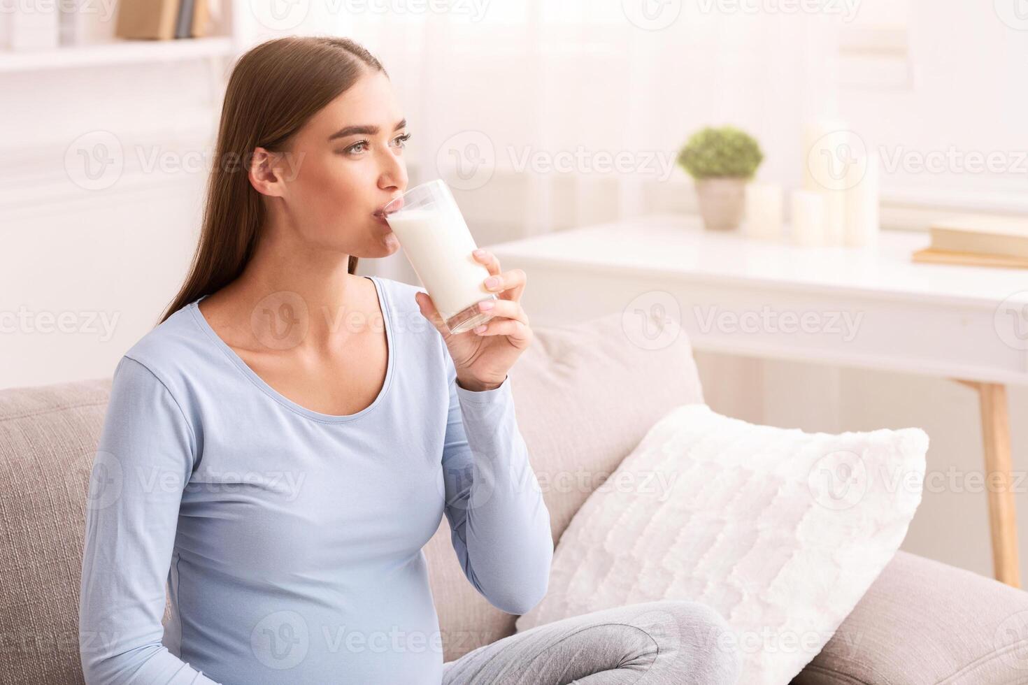 Dairy In Pregnancy. Pregnant Young Woman Drinking Milk Sitting On Couch At Home. Free Space photo