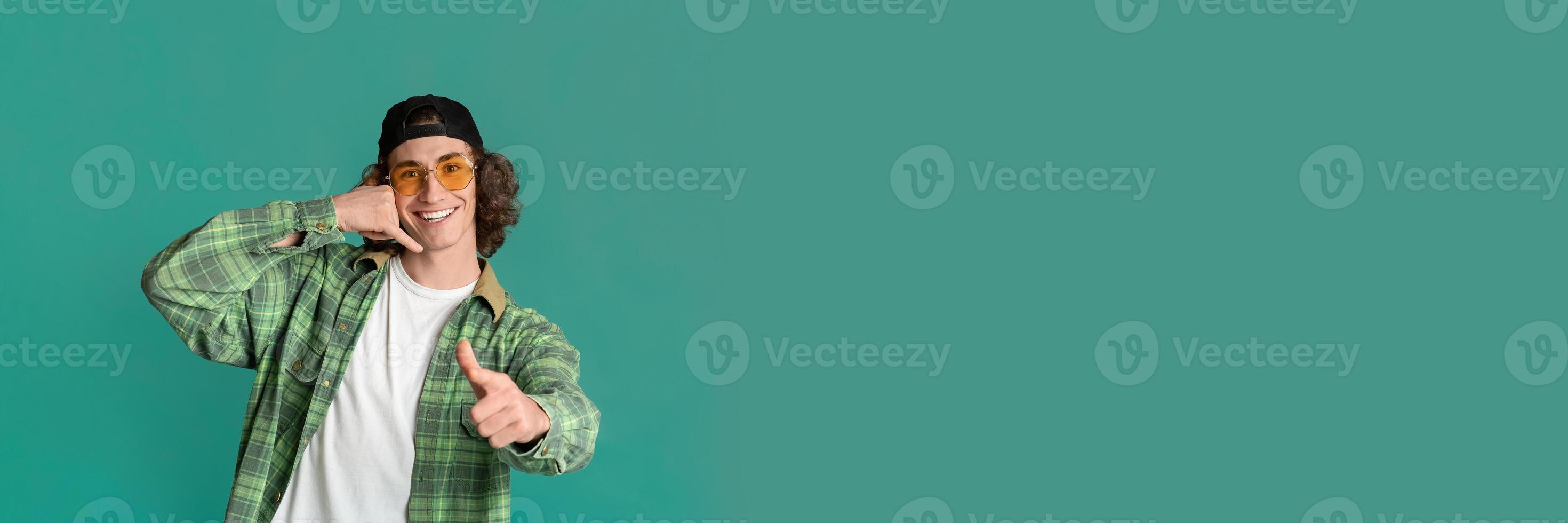 Portrait of confident curly teenager pointing at you and gesturing CALL ME on turquoise background, panorama with copy space photo