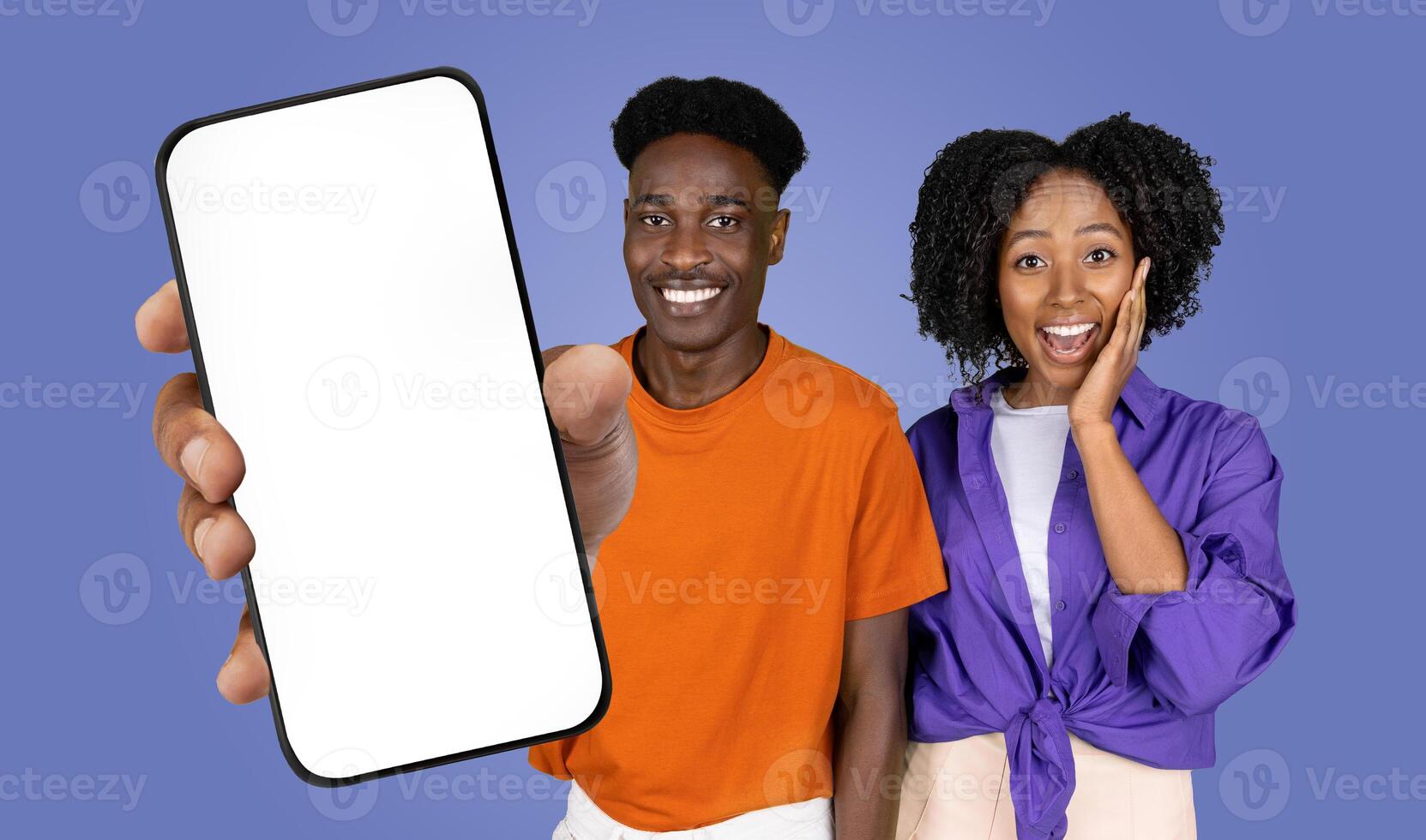 African American man and woman are standing side by side in front of a blue background. The man is holding out a smartphone with a blank screen towards the viewer photo