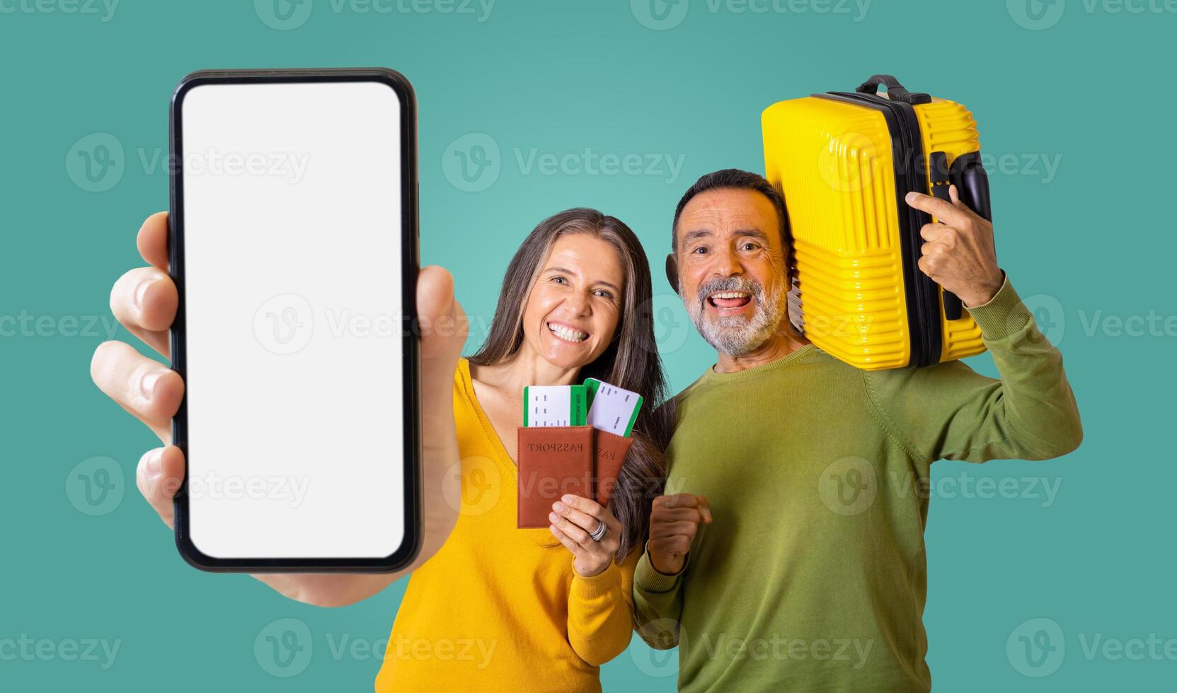 Mature couple stand in front of a green background. The woman holds smartphone with blank screen, passport and tickets, while the man holds a yellow suitcase photo