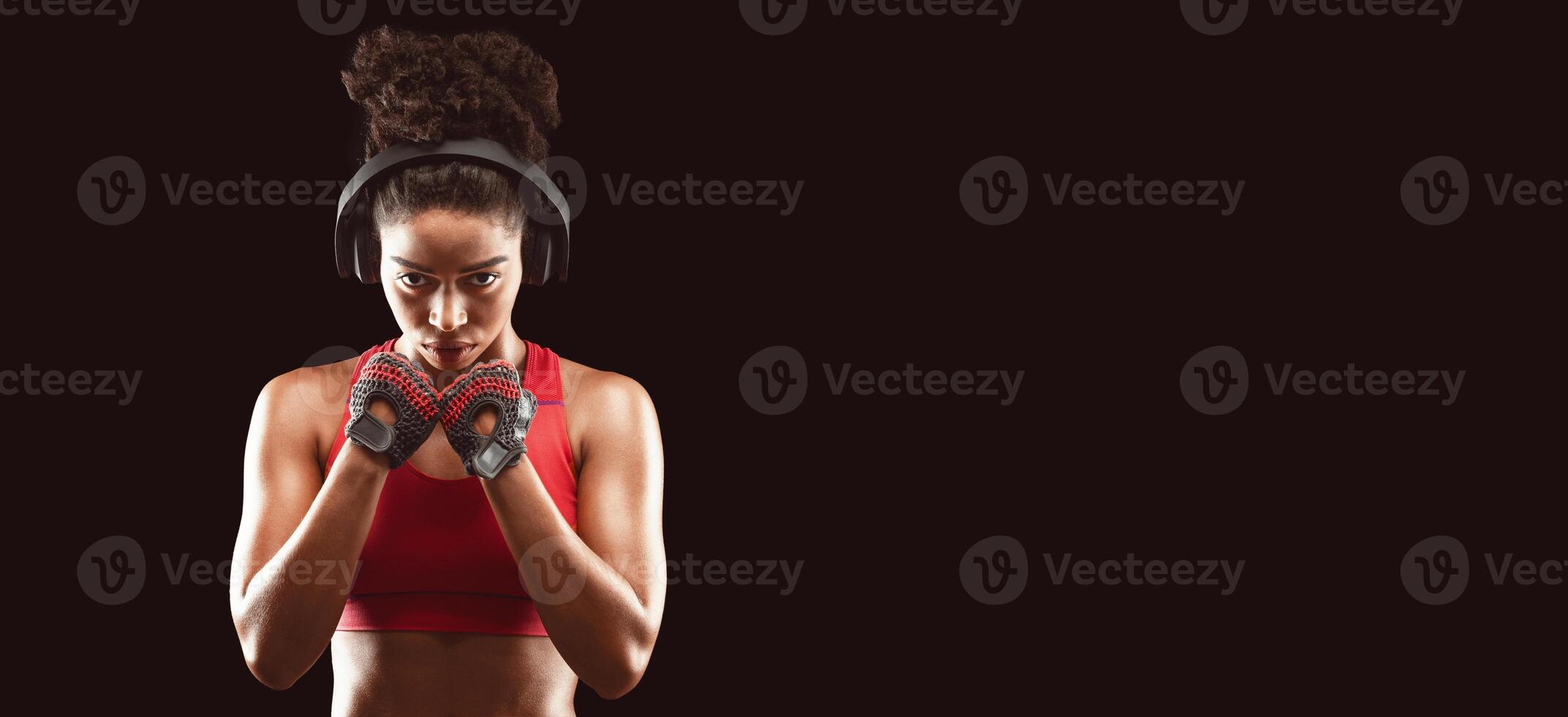 Portrait of beautiful african athletic woman with perfect muscular body wearing gloves and listening to music during training. Active, healthy lifestyle concept photo