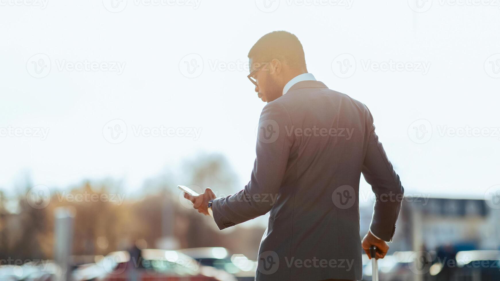 Black man business traveler is on the phone outside a contemporary airport. The mood is efficient and focused, showing the blend of travel and work in a sleek environment. photo