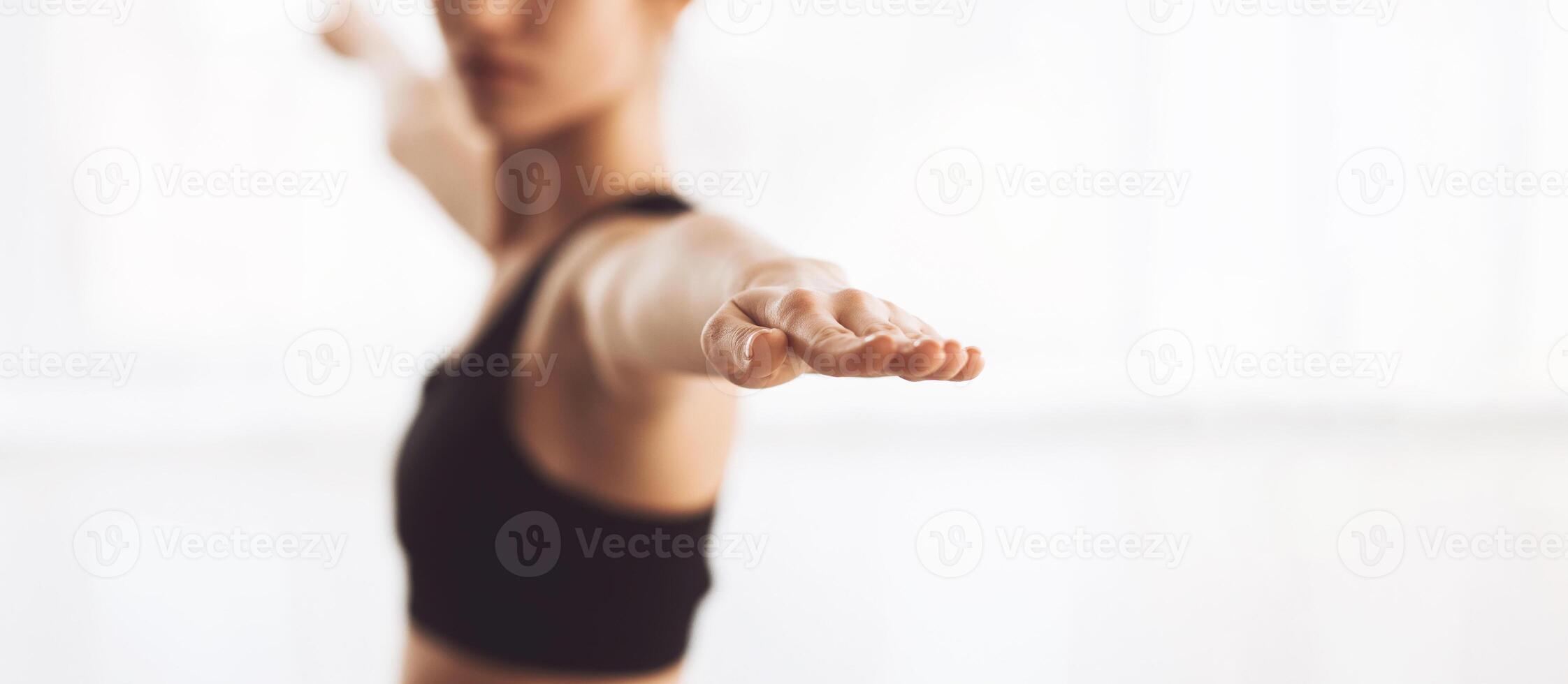 A person is practicing yoga inside a bright, airy space. The individual is in a focused stance, stretching their arms outward, which indicates they are engaging in a balancing pose, copy space photo