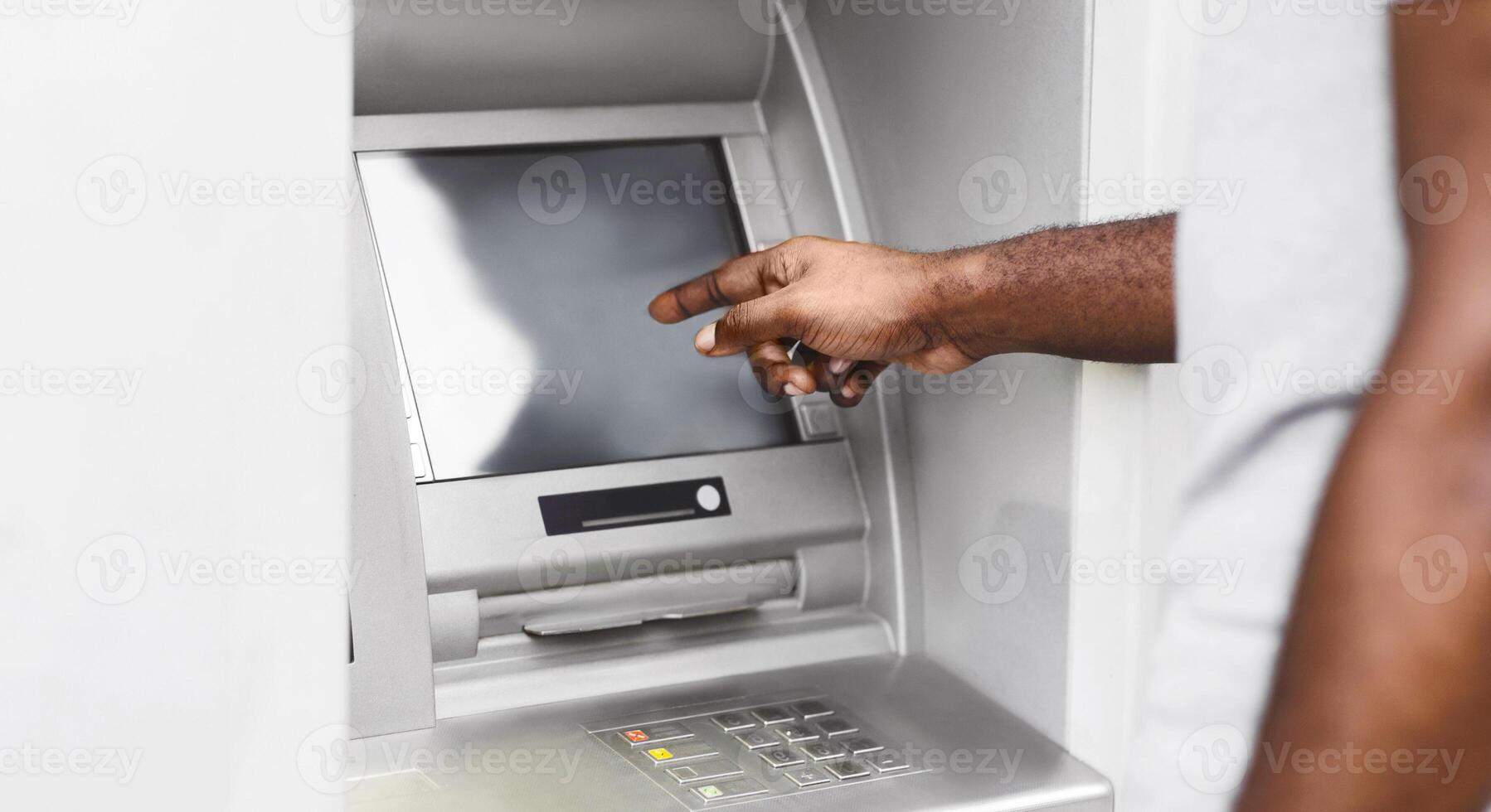 A close-up of a persons hand interacting with an ATM screen. The persons arm and shoulder are visible in the background. photo