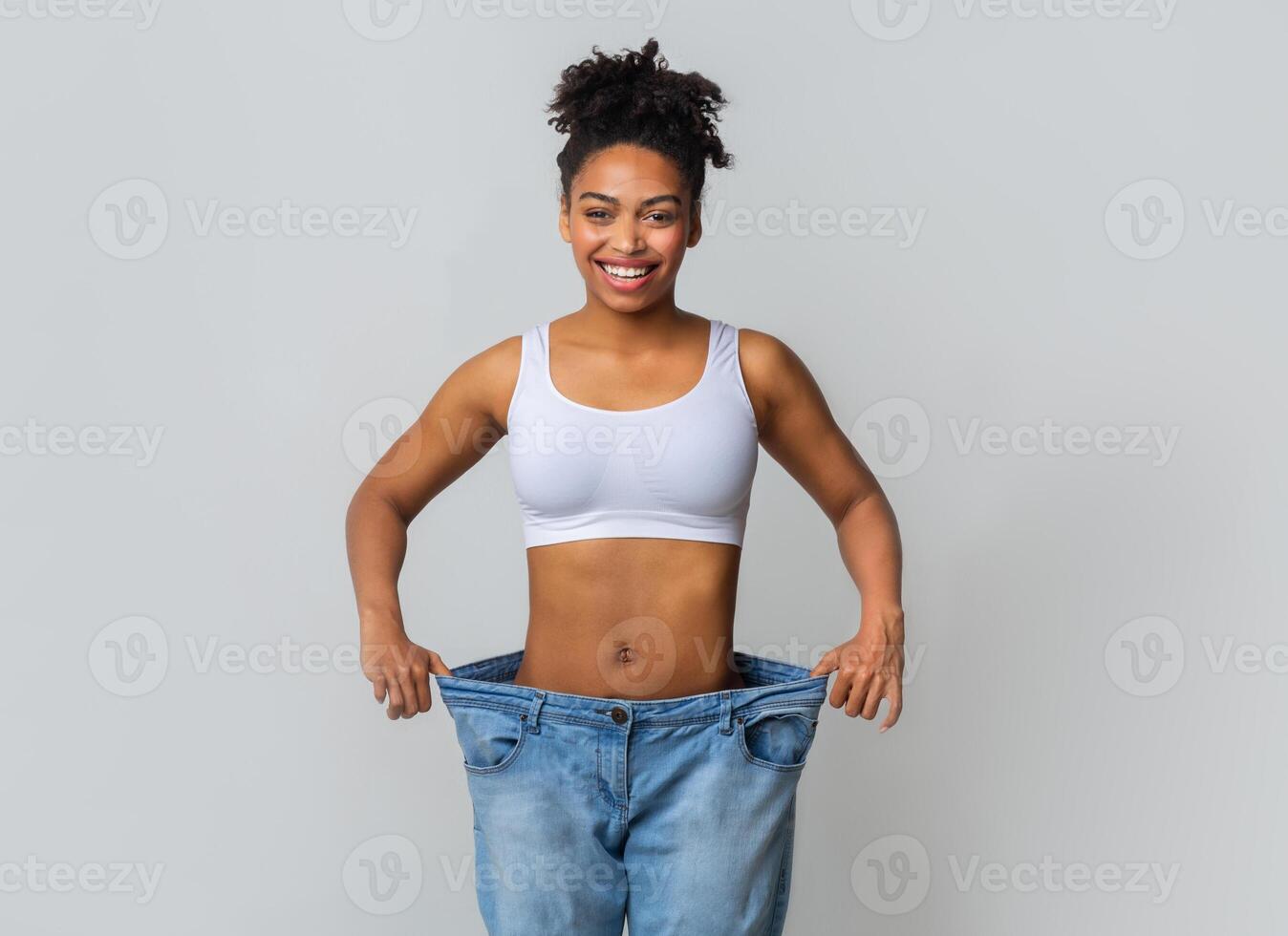 Successful weight loss, afro woman with too large jeans after effective diet, grey background photo