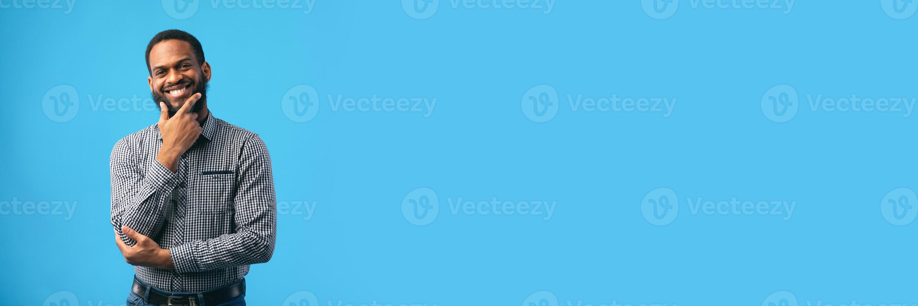 Making Decision. Thoughtful black guy looking at camera, holding hand on chin, isolated over blue wall, copy space, web-banner photo