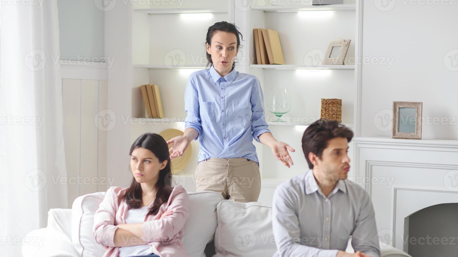 A therapist is seen mediating an intense discussion between a couple seated on a sofa in a modern living room. The couple looks upset as the therapist attempts to facilitate communication photo