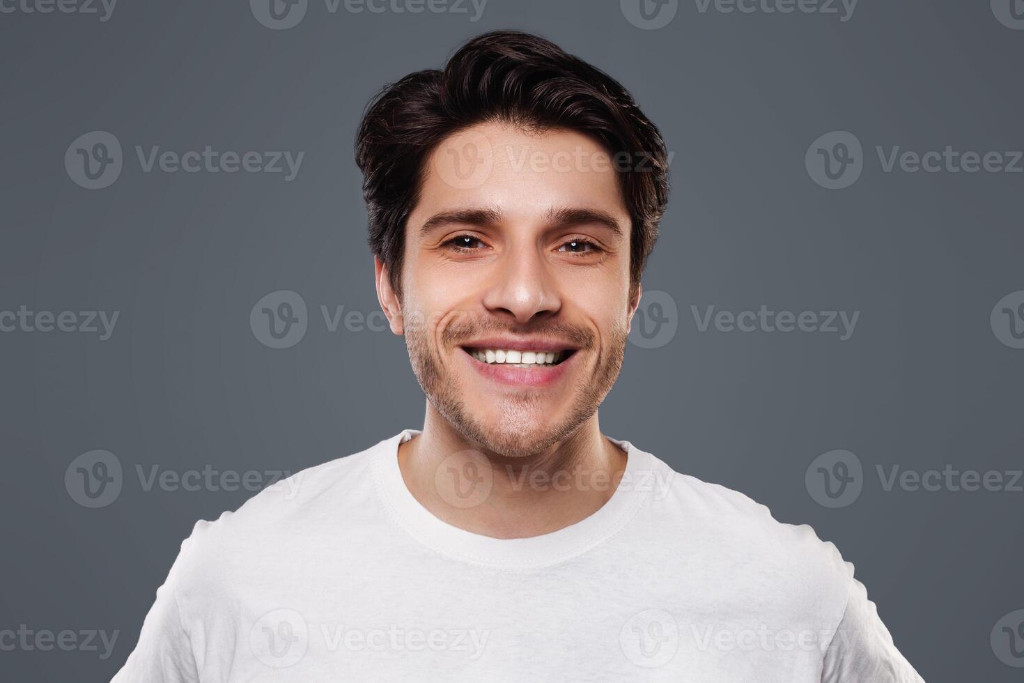Handsome young man smiling at camera on grey background photo