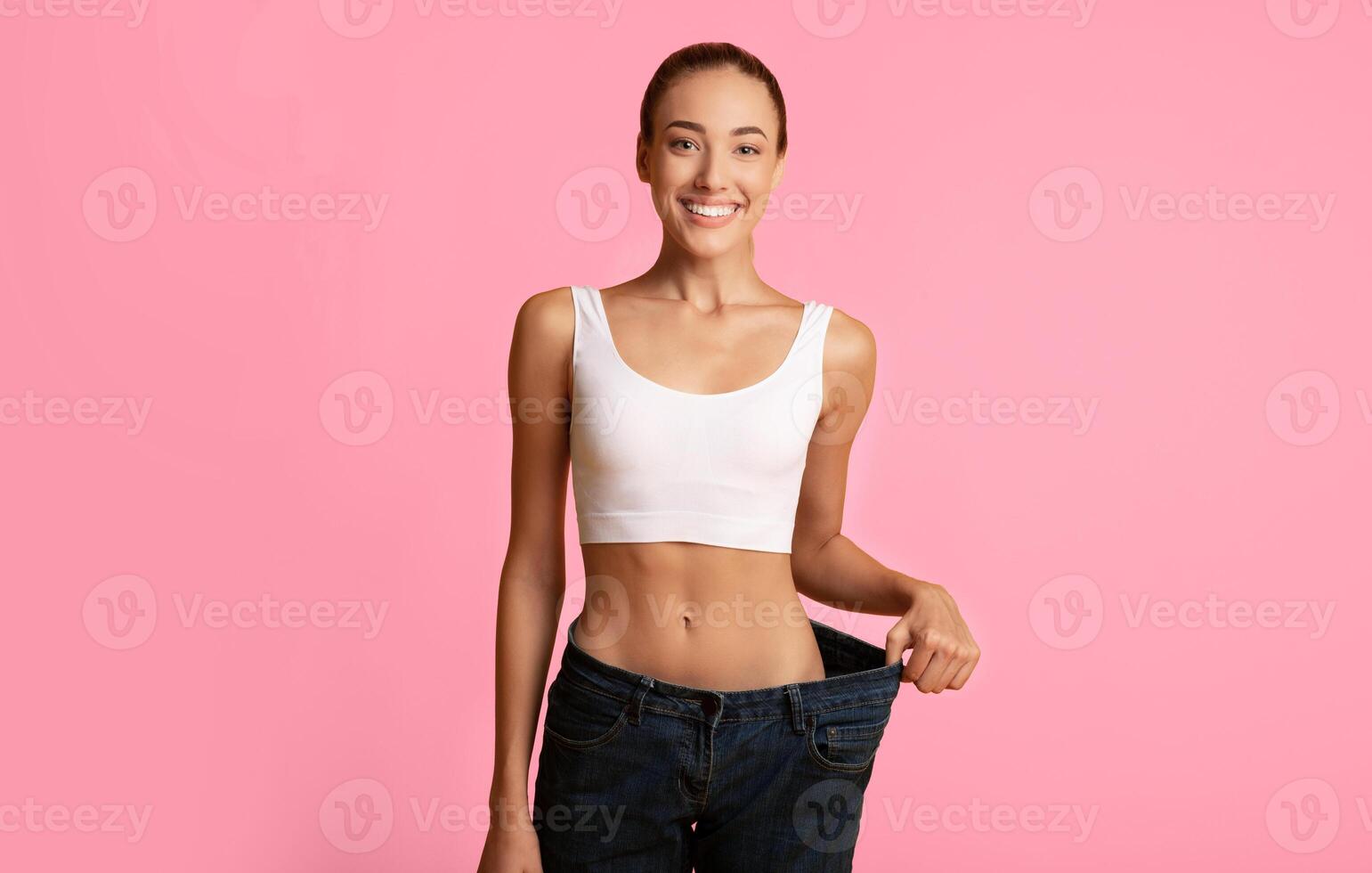 Weight Loss Concept. Slim Girl In Oversize Jeans Standing On Yellow Studio Background. Copy Space photo