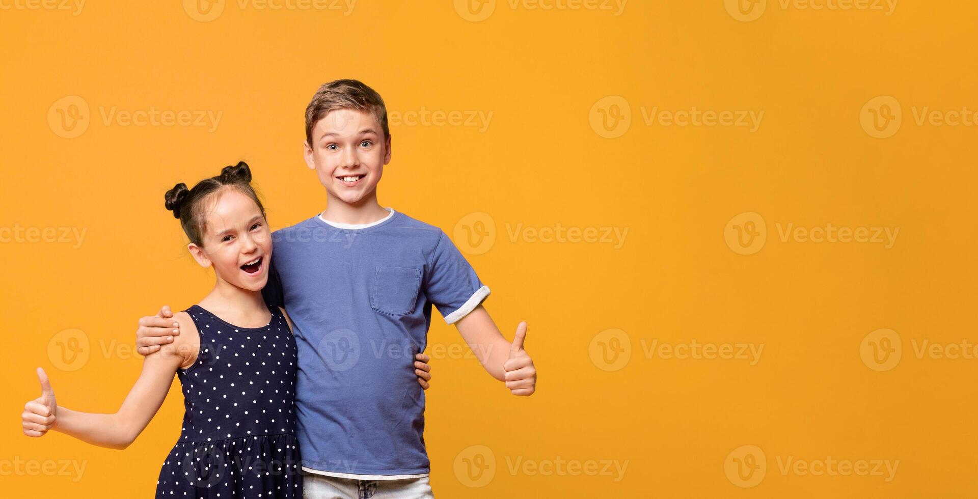Approved by kids. Cheerful little boy and girl showing like gesture, orange studio background photo