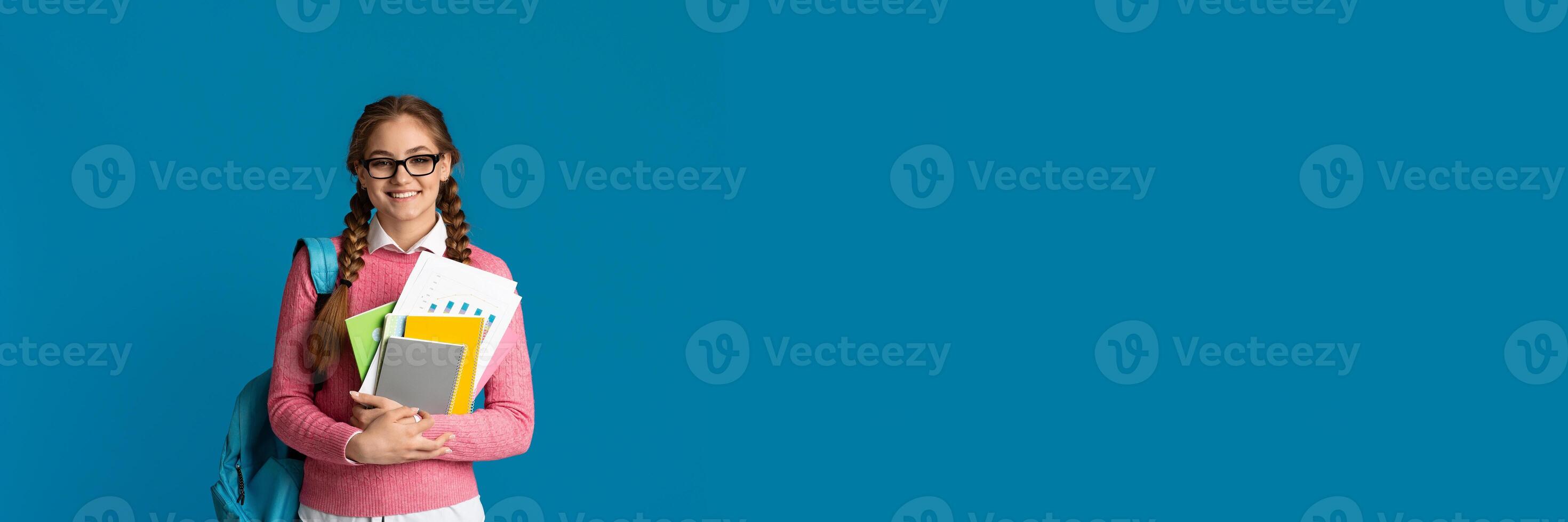 Modern student concept. Cute smiling girl teenager with notebooks and backpack posing on blue studio background, copy space photo