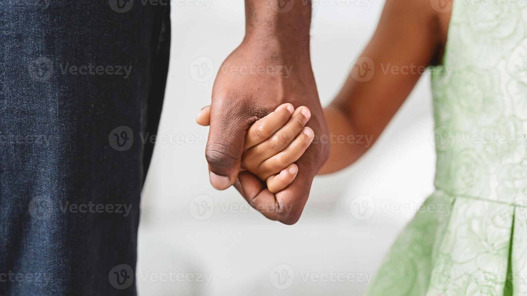A close-up image of a father and daughter holding hands. The fathers hand is larger and darker, while the daughters hand is smaller and lighter photo