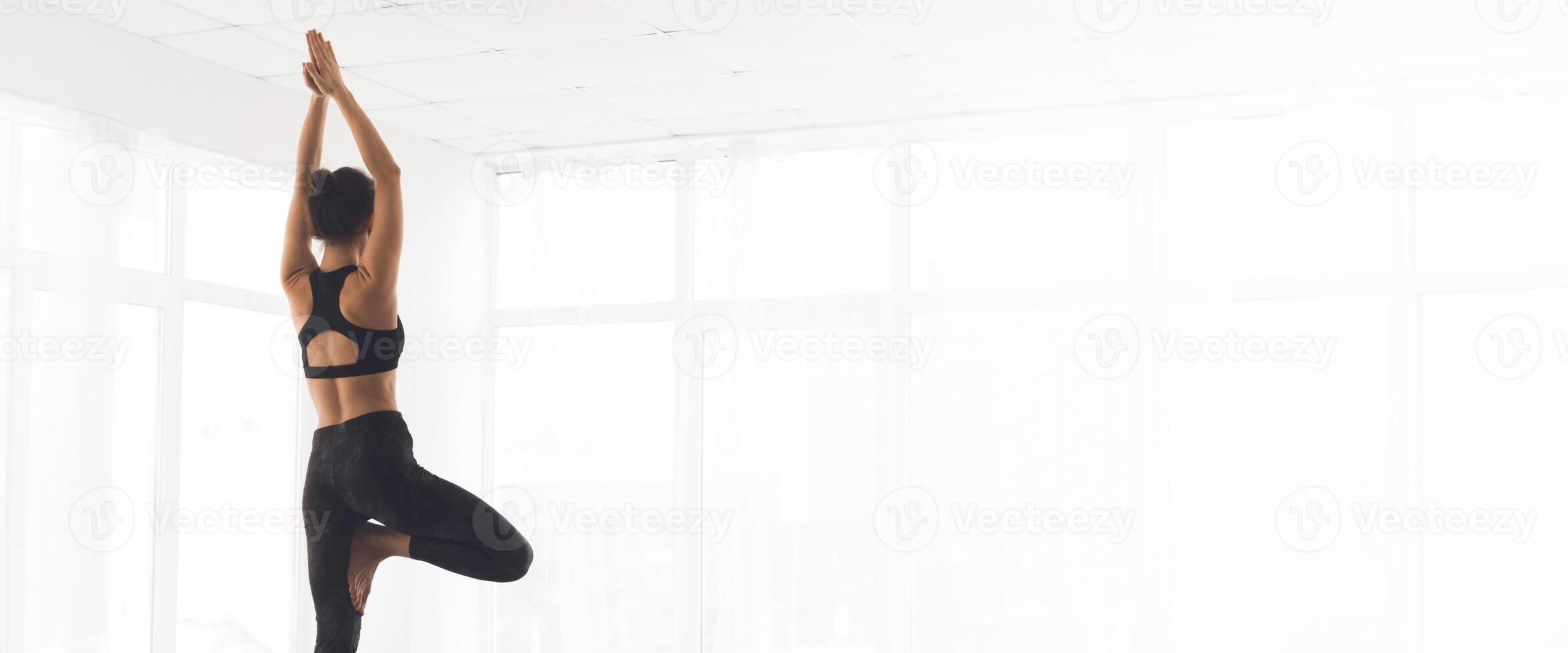A woman balances gracefully on one leg while practicing yoga in a sunlit studio, copy space photo