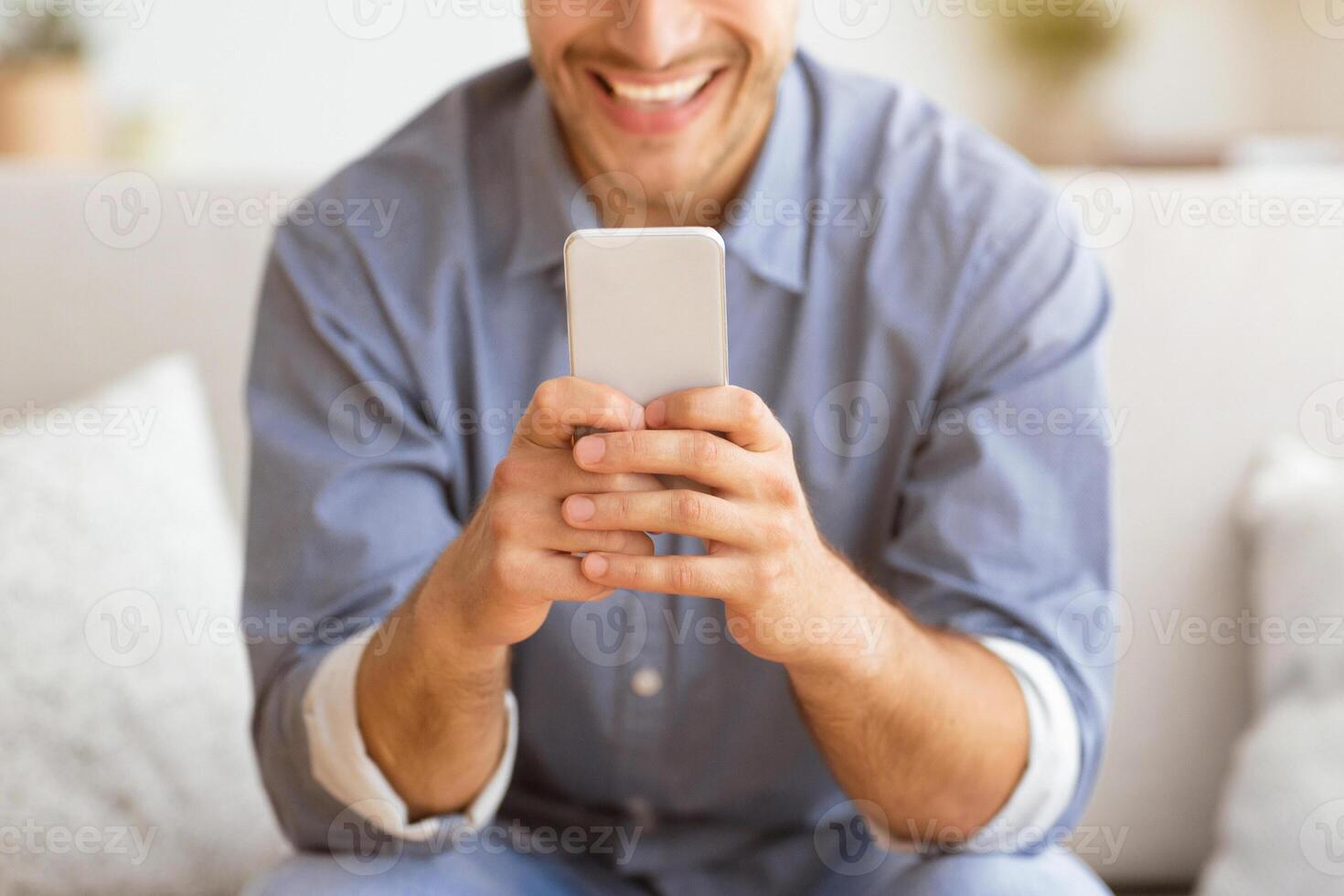 Happy Man Texting at Phone. Guy Playing On Smartphone Sitting On Sofa At Home photo