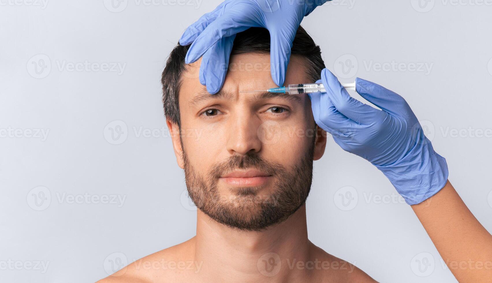 A man receives an injection to his forehead from a doctor wearing blue gloves. photo
