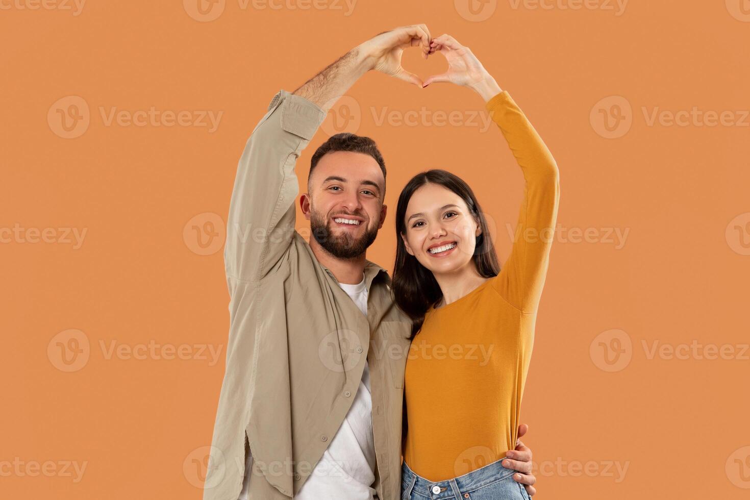 A man and a woman standing close to each other, joining their hands to form a heart shape. The mans right hand and the woman left hand are positioned in a way that creates the iconic heart symbol photo