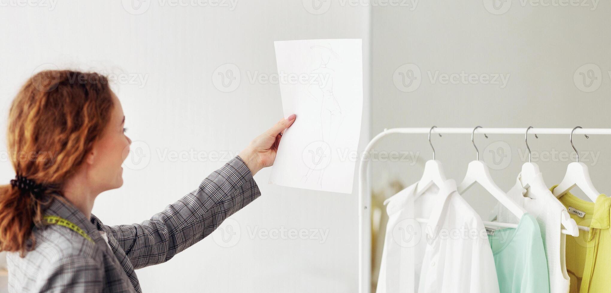 Fashion entrepreneur checking new sketches drawn on sheets of paper, working in atelier photo