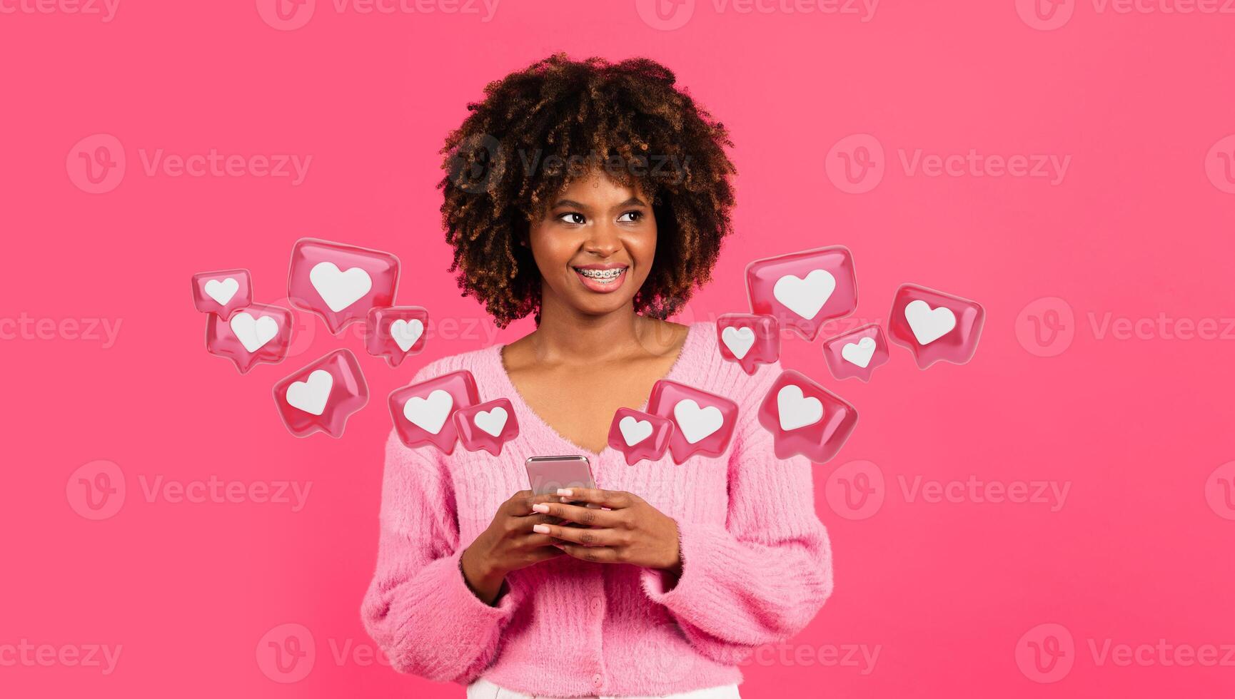 contento milenario africano americano Rizado mujer con tirantes en casual mecanografía en teléfono en rosado fondo, estudio, chateando con amante foto