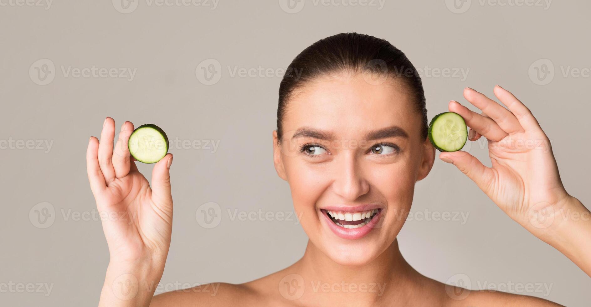 A woman is playfully holding two cucumbers up to her face, creating a humorous and lighthearted moment. The cucumbers are fresh and vibrant, contrasting with her skin tone. photo
