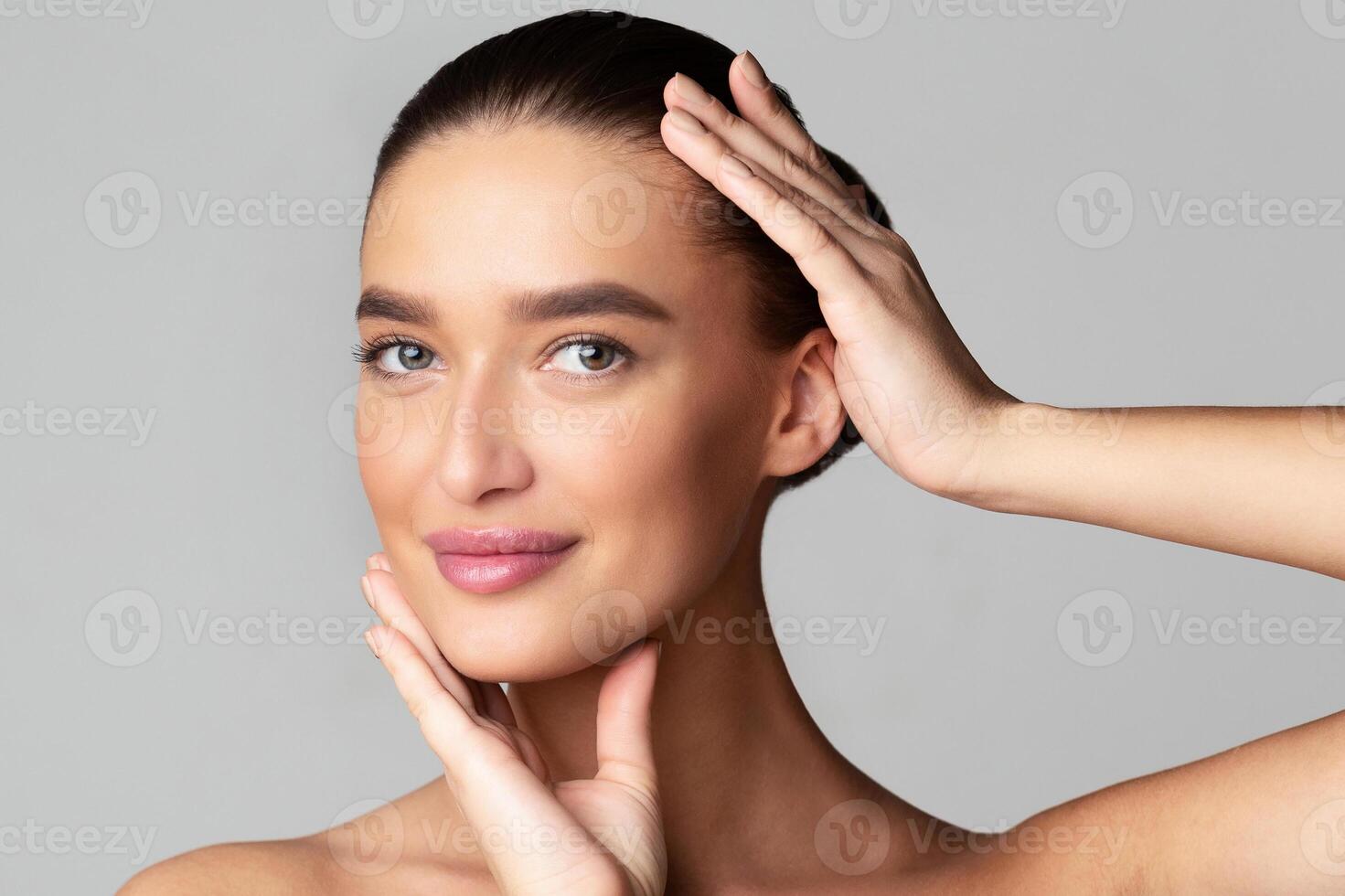 Closeup of woman is standing with her hands on her face, appearing thoughtful or contemplative. She is looking directly at the camera, showcasing a pose that conveys introspection and emotion. photo