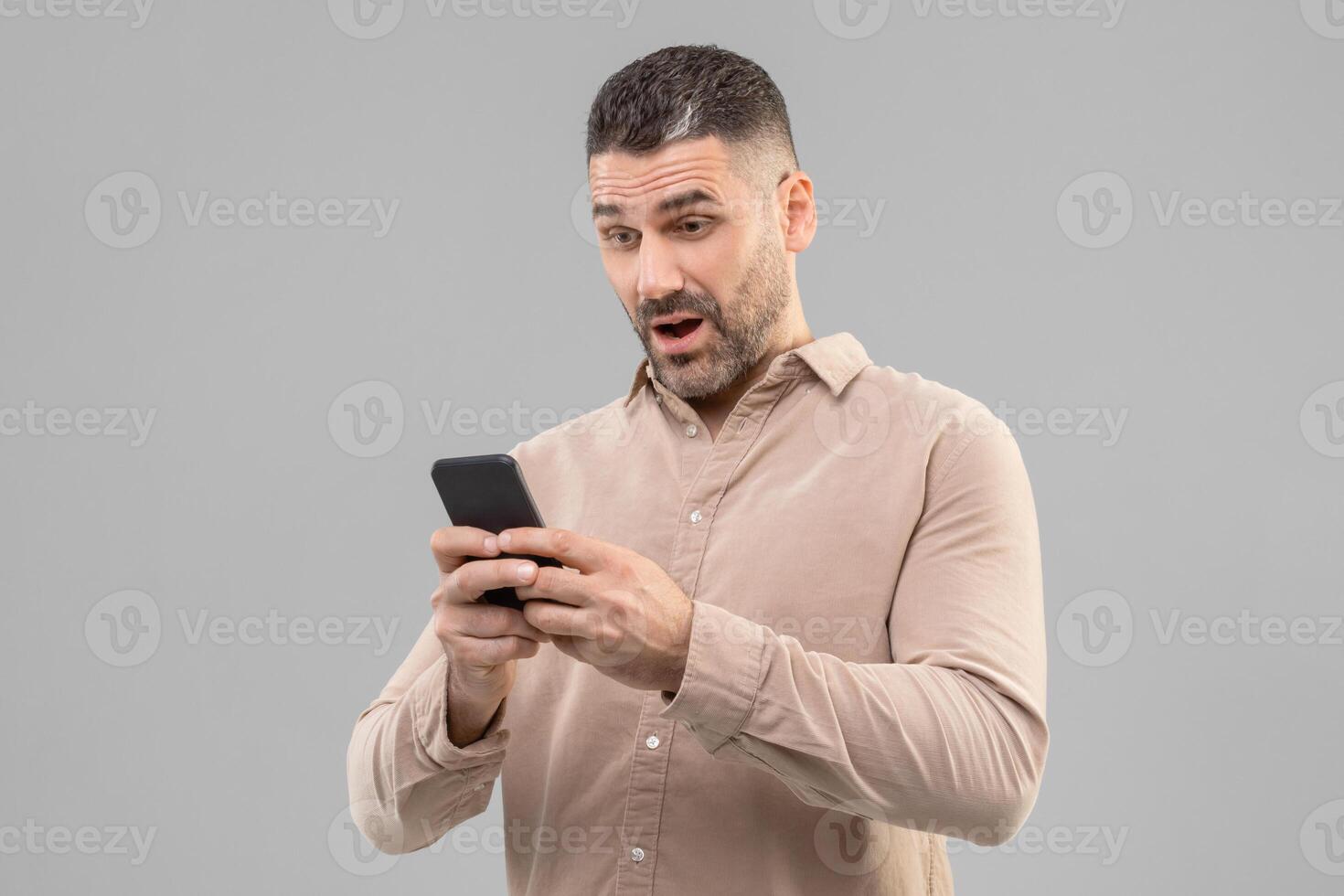 Surprised man with short hair holding a smartphone in his hand, looking down at the screen. He appears focused on using the device. photo