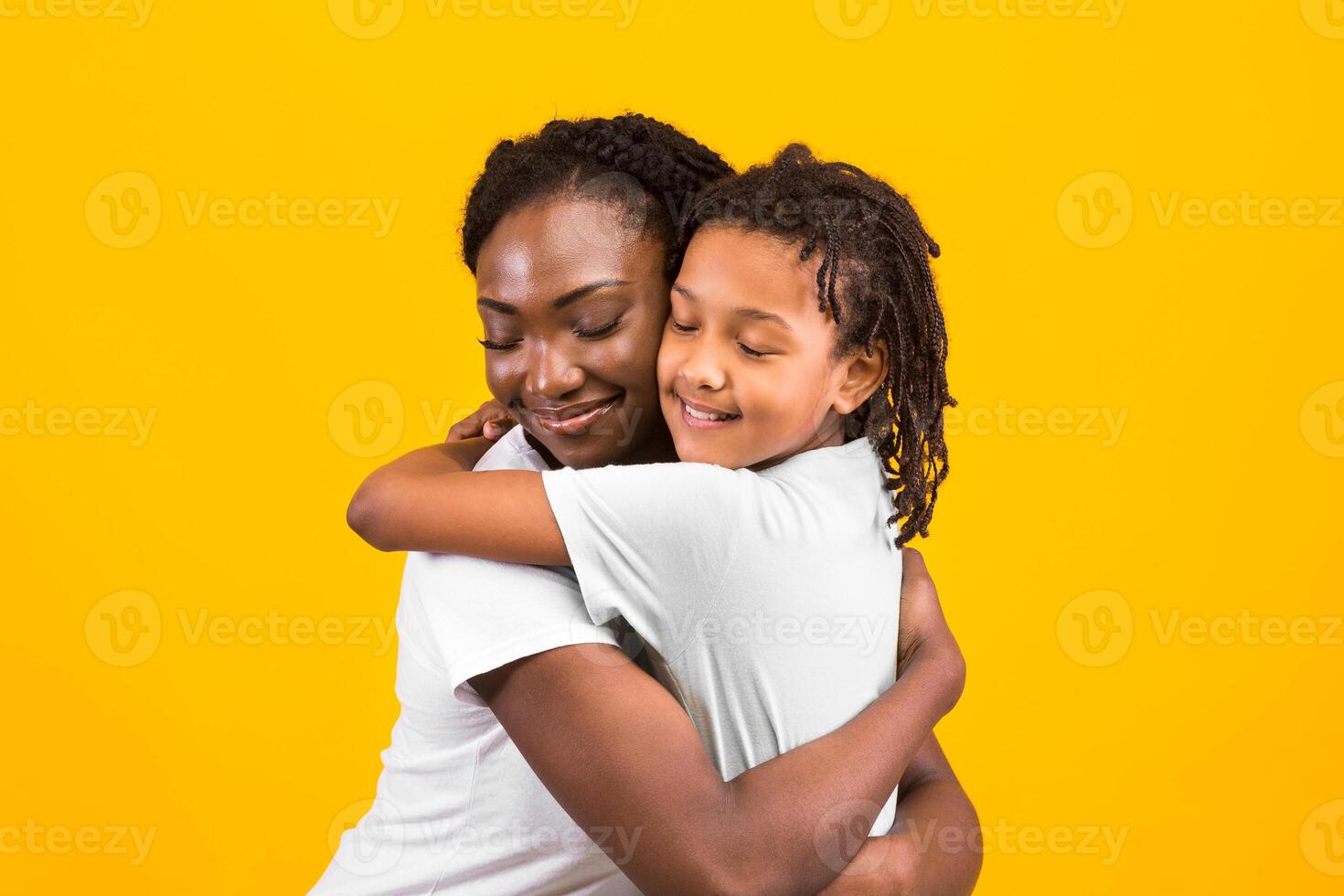 Loving African Woman Embracing Her Child, Looking Happy And Calm. Yellow studio wall, copy space photo