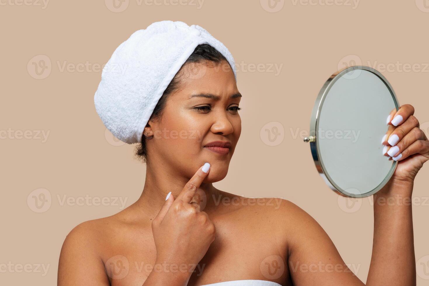A woman is standing in front of a mirror, closely examining her own face. She appears focused and engaged, likely inspecting her skin or features. The mirror reflects her image back at her. photo