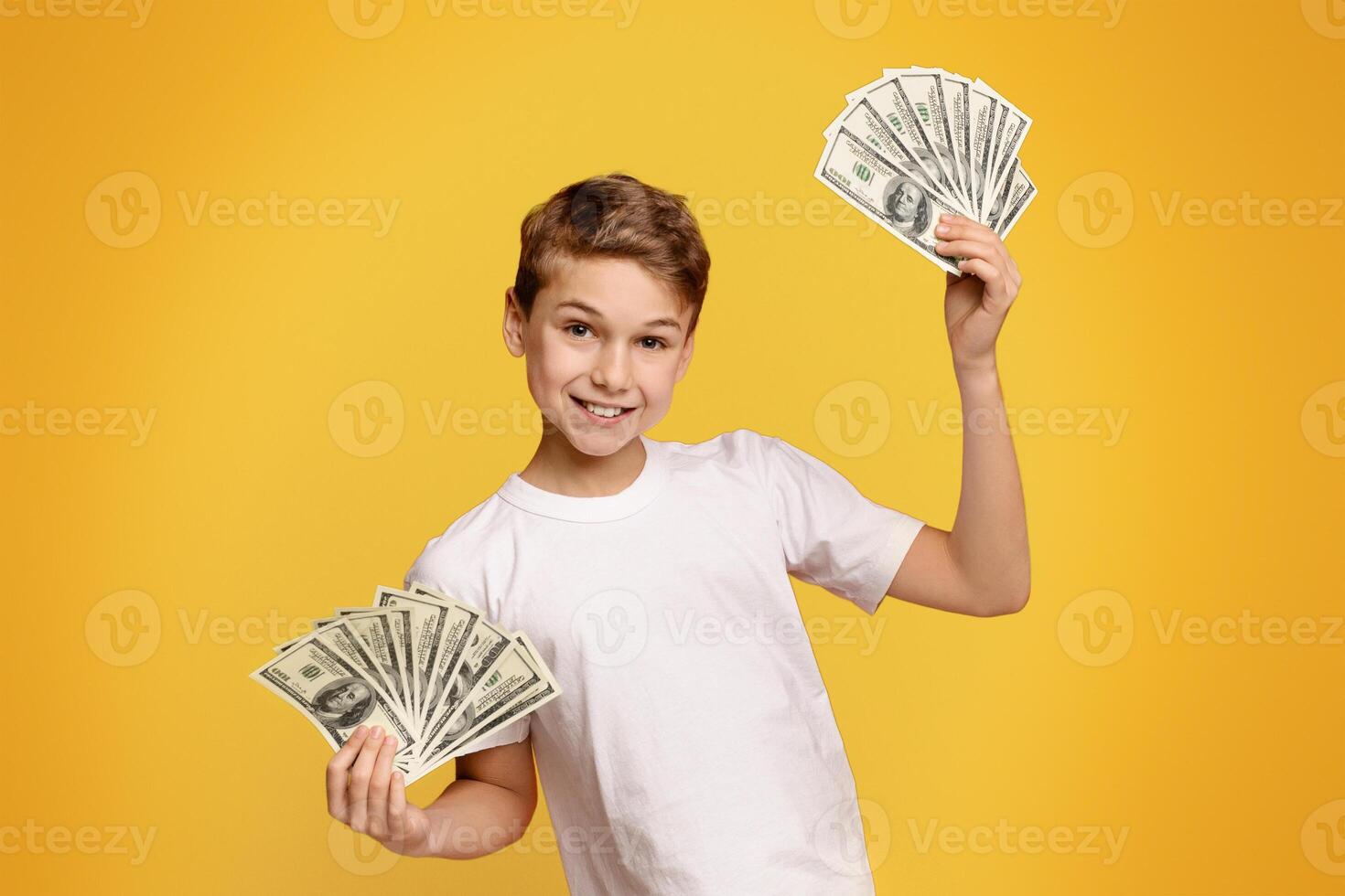 Saving money concept. Happy teen boy holding bunch of money, orange background photo