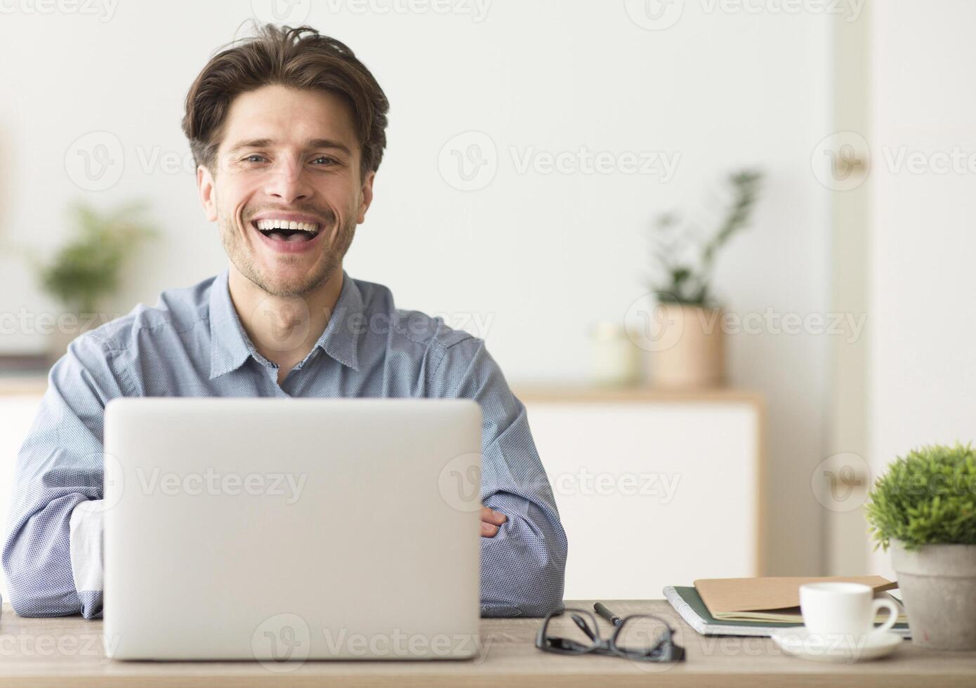 Man Sitting At Laptop And Laughing Looking At Camera Indoor. Empty Space For Text photo