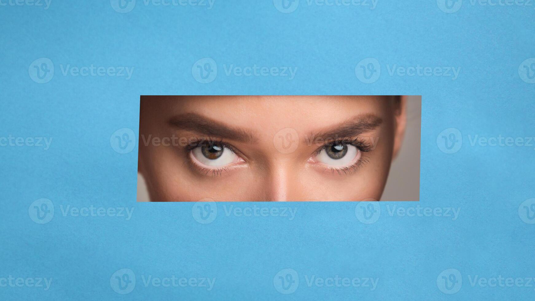 A close-up of a woman eyes with a neutral expression, set against a solid blue background. The woman features are in focus, showing fine details like her eyes, nose photo