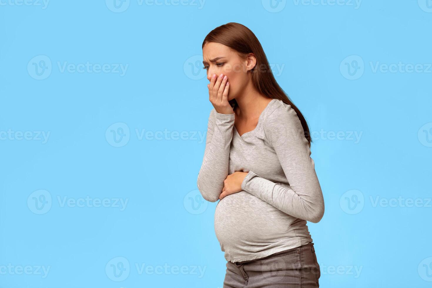 Toxicosis Of Pregnancy. Pregnant Lady Feeling Sick Having Nausea Standing On Gray Studio Background. Free Space photo