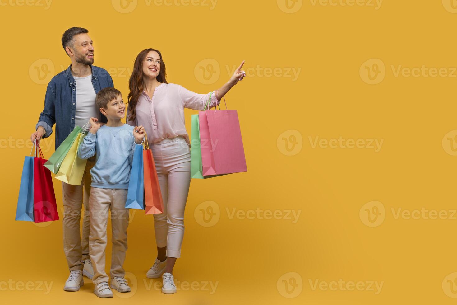 A man and a woman stand holding shopping bags while next to a child, surrounded by a shopping environment. The trio appears to be engaged in a family outing or shopping trip, copy space photo