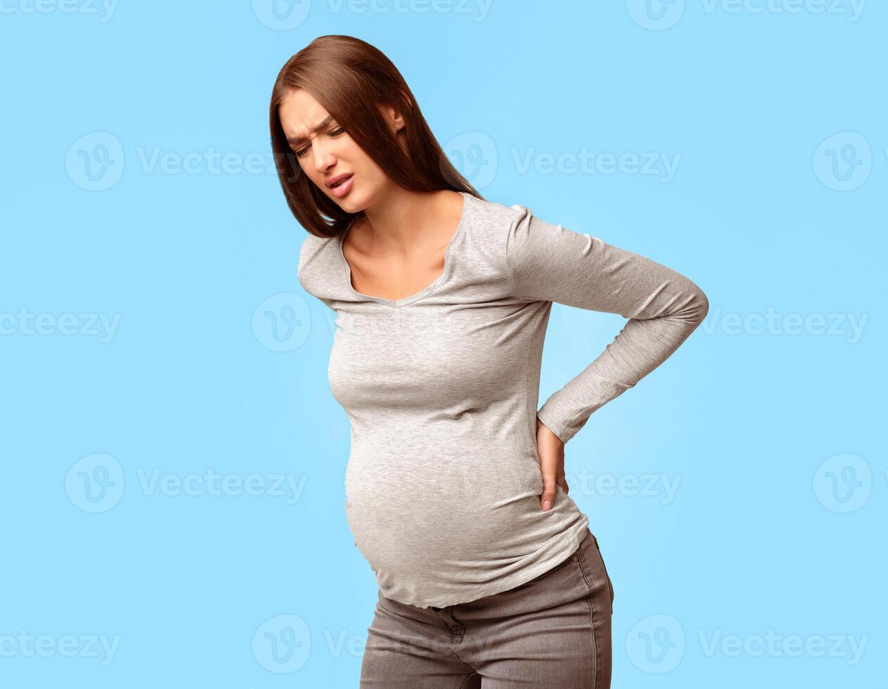 Pregnancy Backache. Pregnant Woman Having Lower Back Pain Standing Over Gray Background. Studio Shot photo
