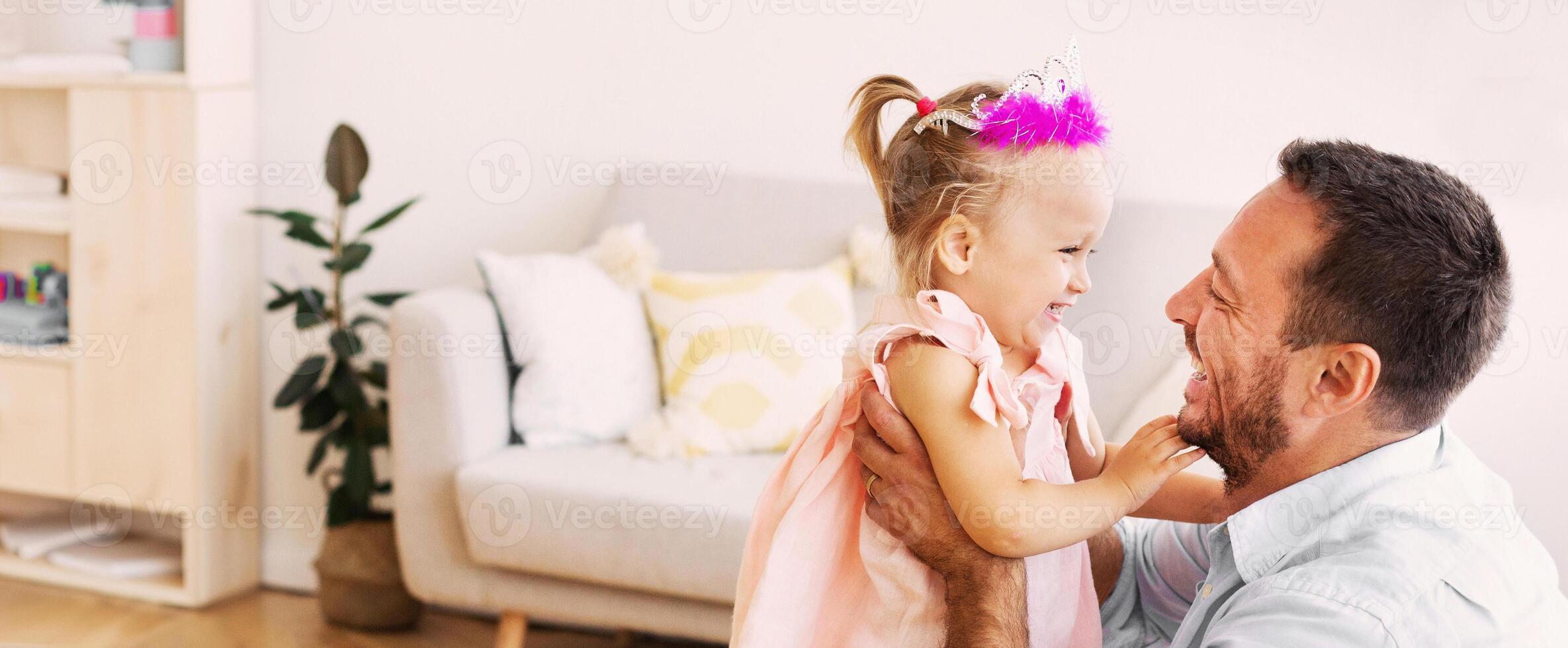 Family Time. Smiling father babysitting his daughter in pink crown. Free space, selective focus photo