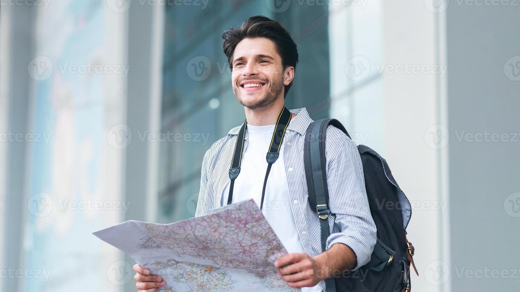 Tourism, summer holidays, active lifestyle concept. Cheerful man traveler holding map, studying new destinations at airport, empty space photo