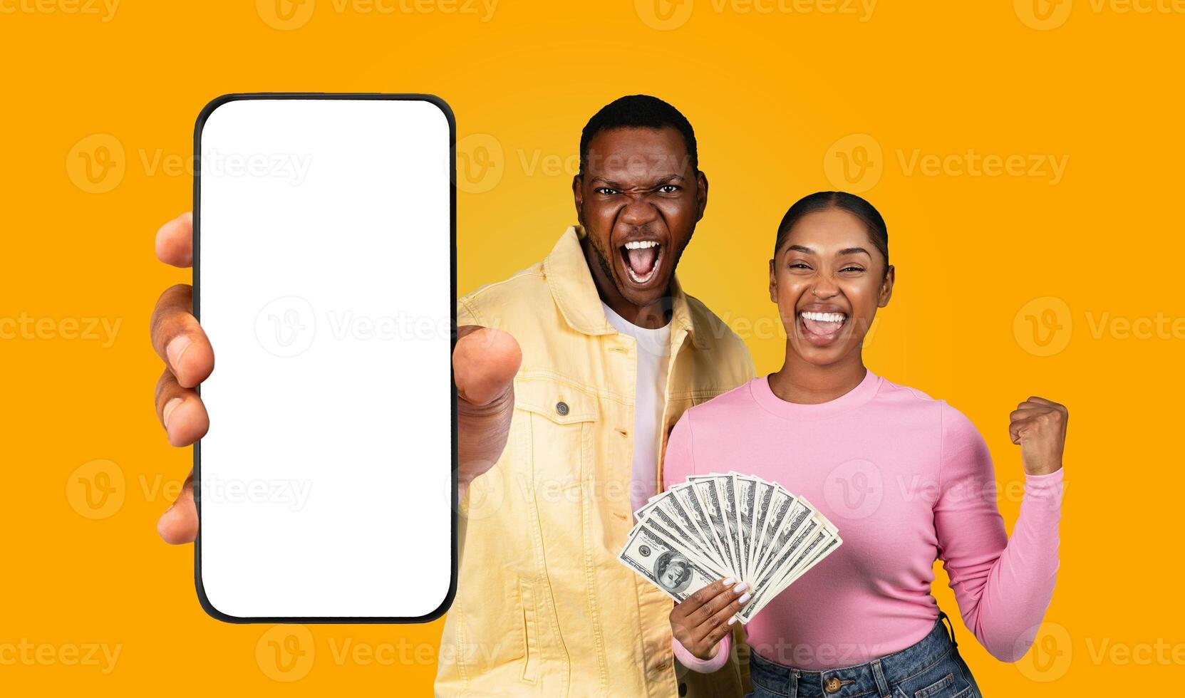 Two black people, a man and a woman, are smiling and holding cash and a smartphone with a blank screen. The man is pointing towards the phone and the woman is holding up a fan of cash photo