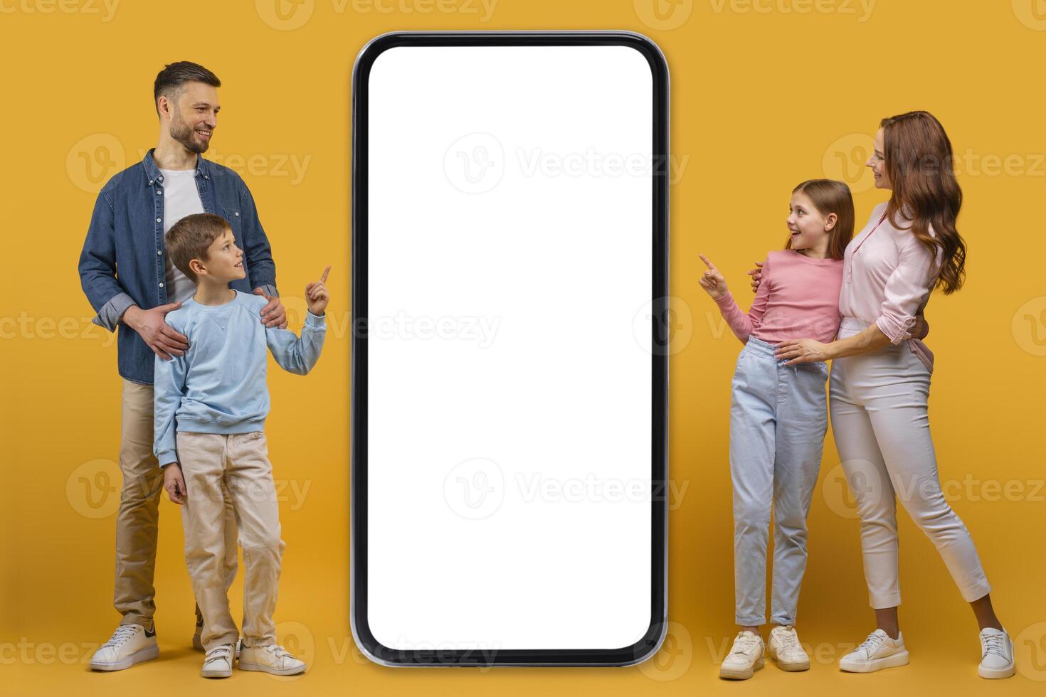 A smiling father, mother, daughter, and son stand together beside an oversized smartphone with a blank screen, possibly interacting with a digital application or advertisement photo