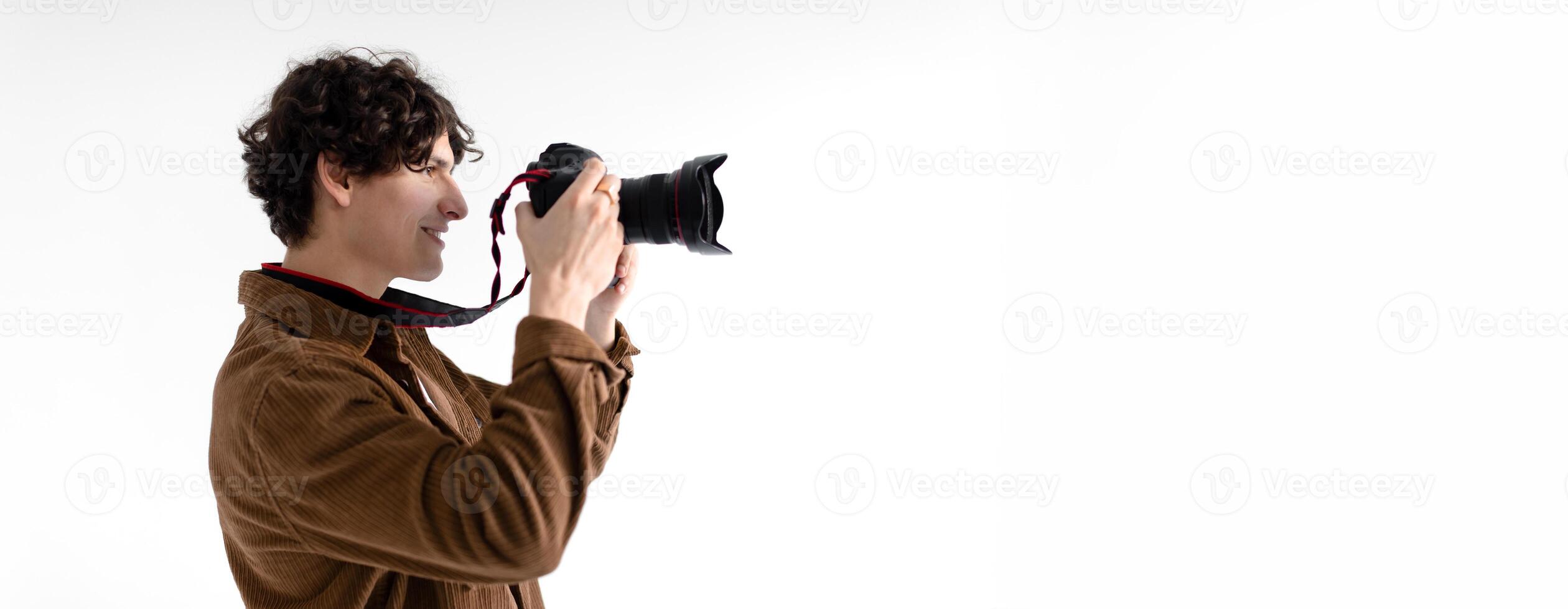 A young man with curly hair is enthusiastically taking pictures using a professional camera in a brightly lit studio. His focus is evident as he aims the lens towards the subject, copy space photo