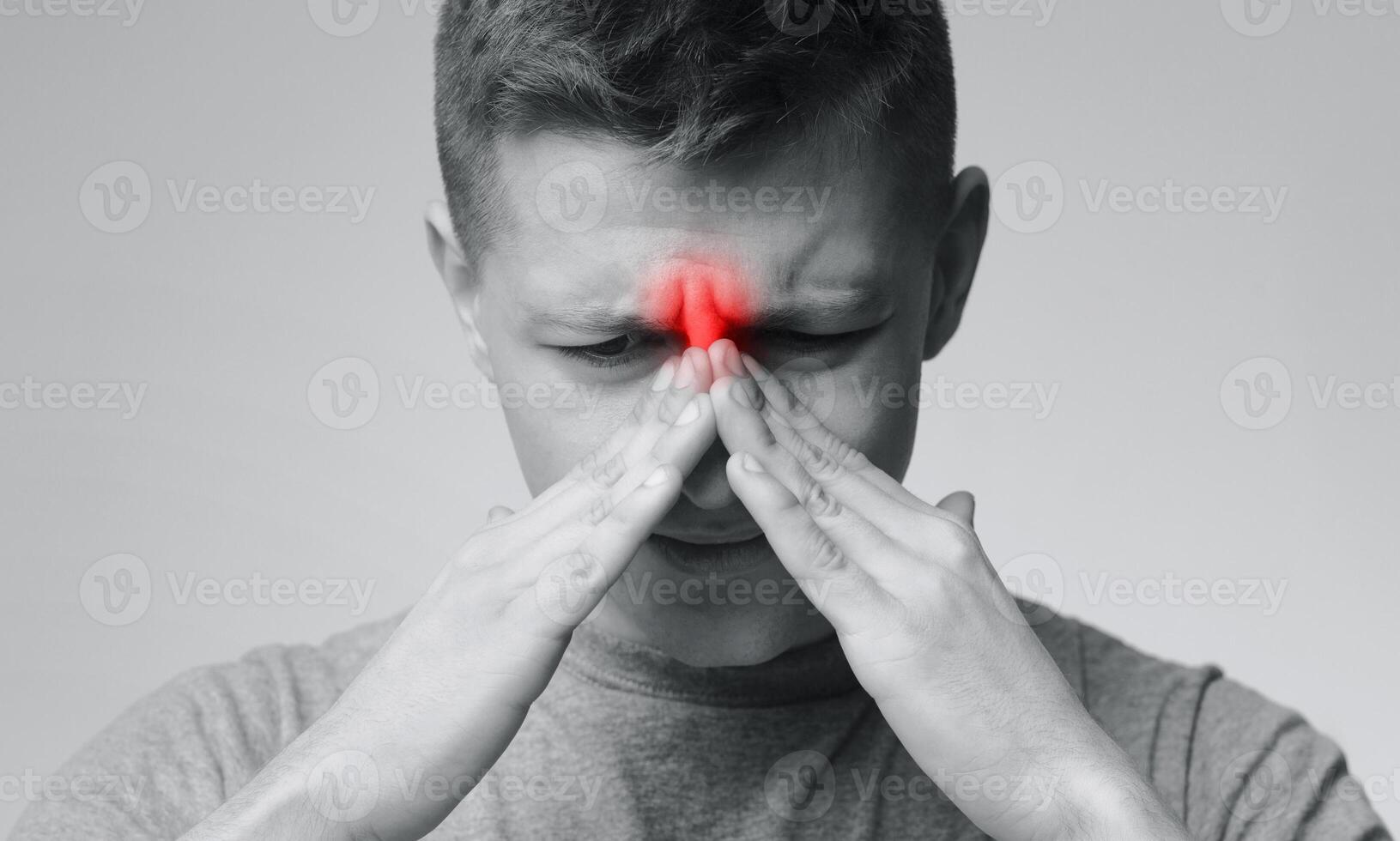 Frustrated young man suffering from sinus pressure, touching his nose with closed eyes, monochrome photo