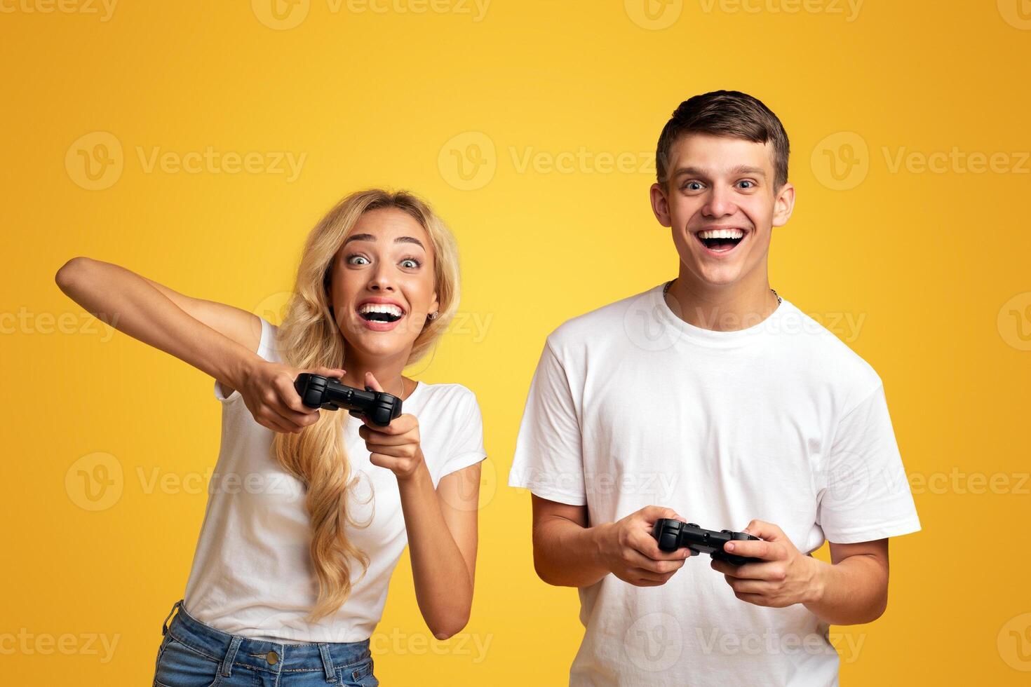 Gambling young couple playing game with joysticks, yellow studio background with copy space photo