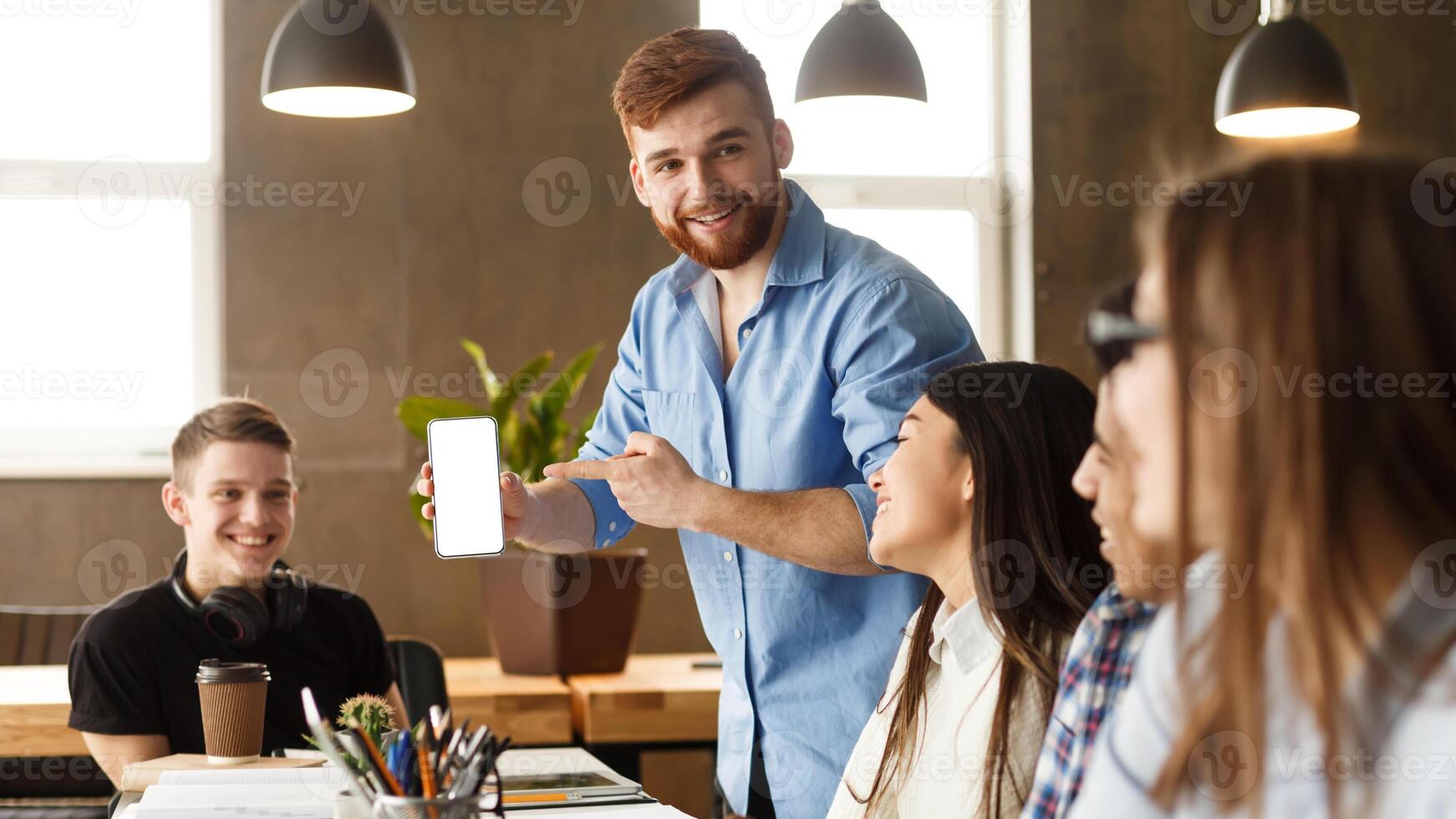 Student guy showing phone with blank screen to classmates, studying together in library photo