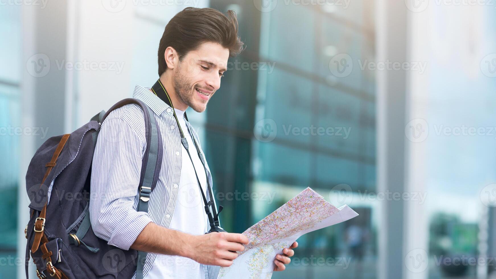 Millennial Tourist. Smiling Man Traveller Standing Near Airport With City Map In Hands, Checking His Route photo